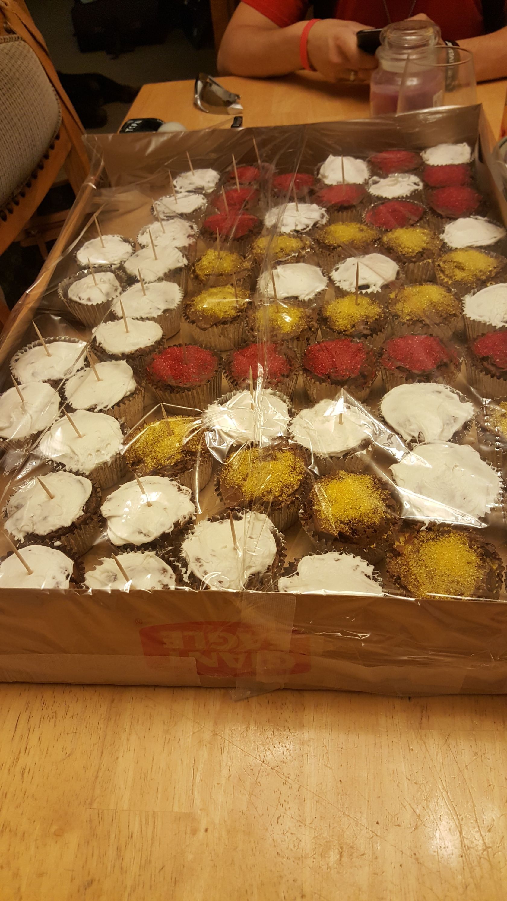 Tray of assorted frosted cookies on a wooden table, with people seated in the background.