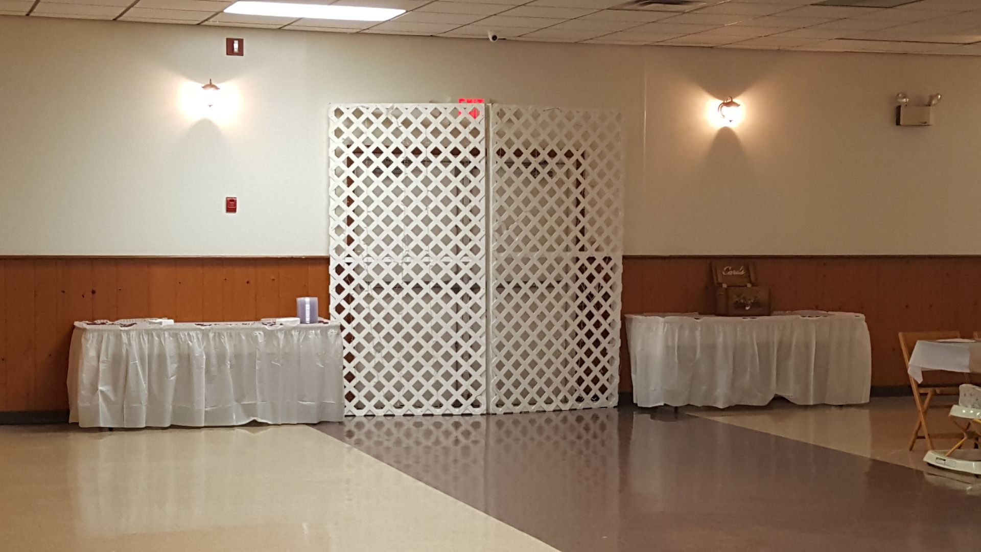 Decorated banquet hall with white lattice backdrop, round tables, and beige walls under warm lights
