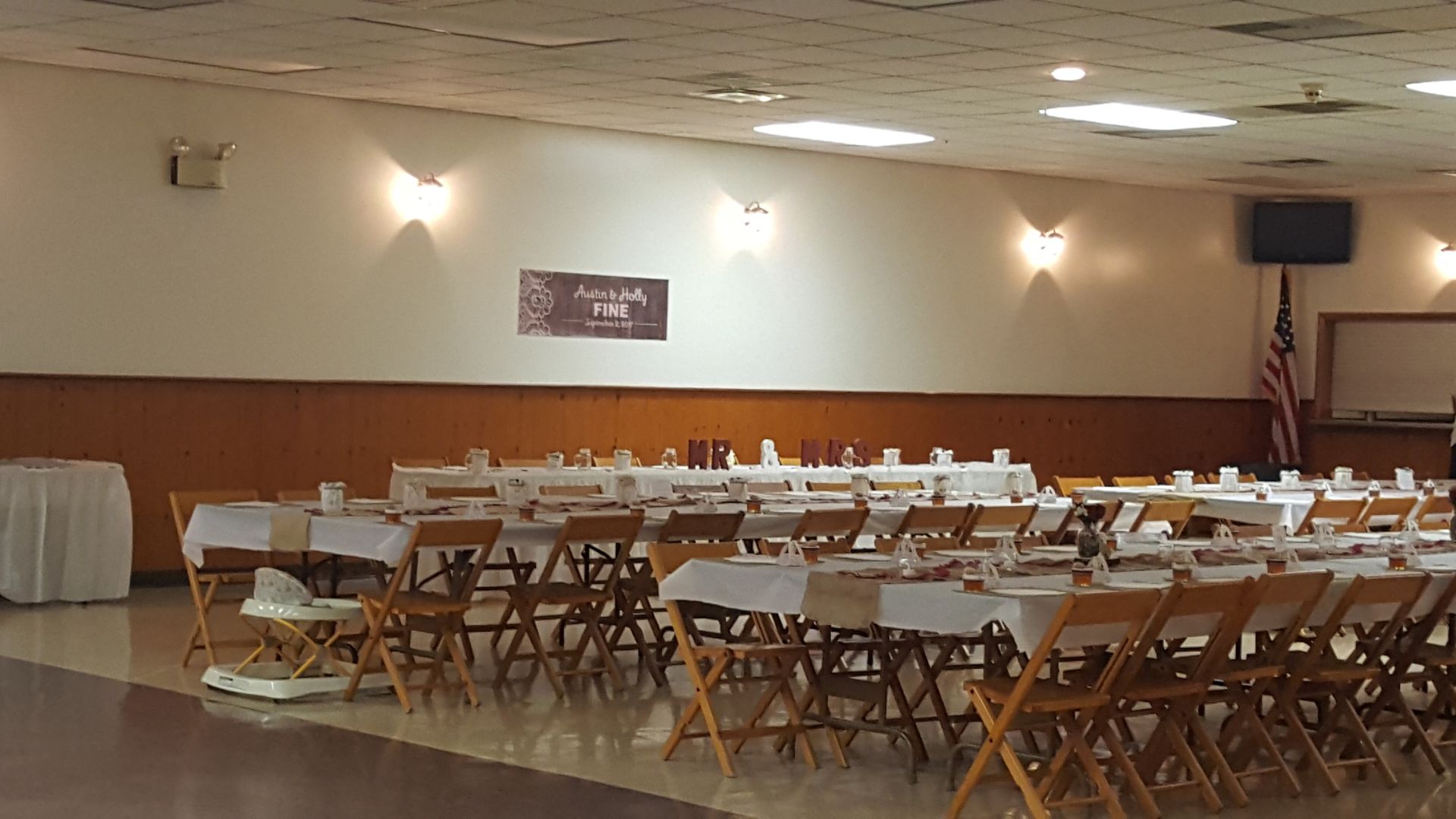 Large banquet hall with rows of folding chairs and tables, beige walls, and an American flag in the corner.
