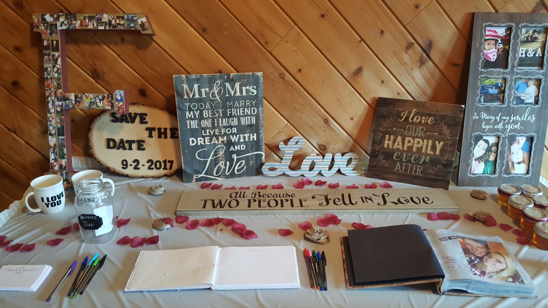 Wood-paneled wedding display table with candles, signs, flowers, and framed photos; “Love” centerpiece