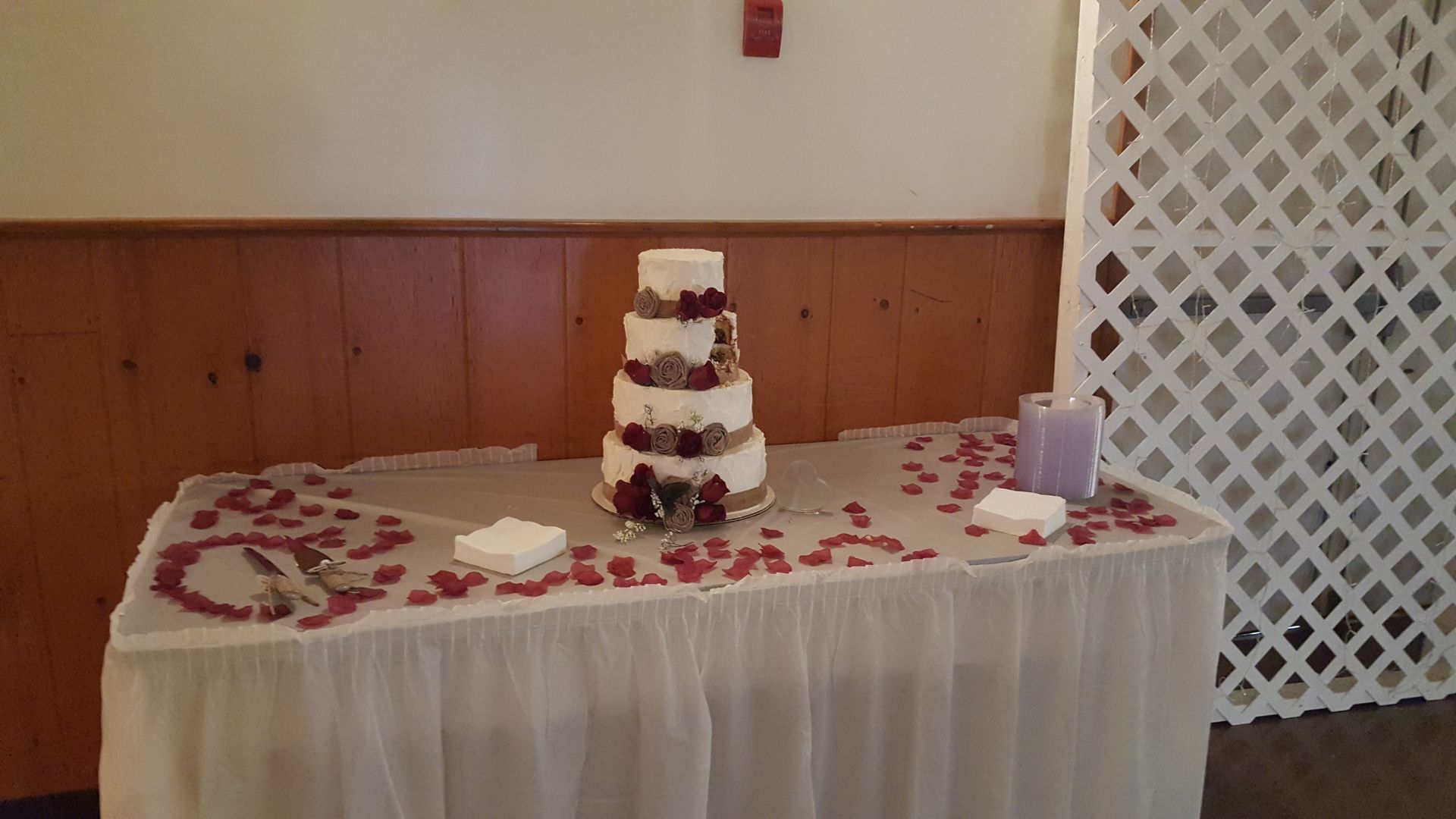 Decorated dessert table with a tiered cake, purple candles, and scattered flower petals at a banquet hall