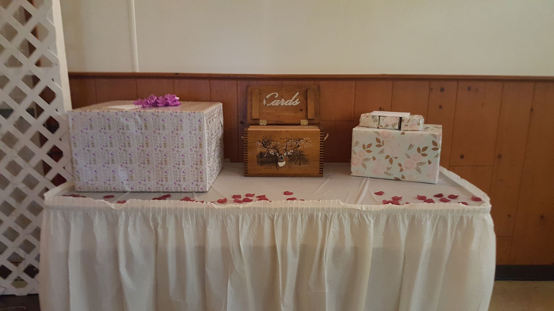 Three wrapped gift boxes on a white-draped table against wood-paneled wall