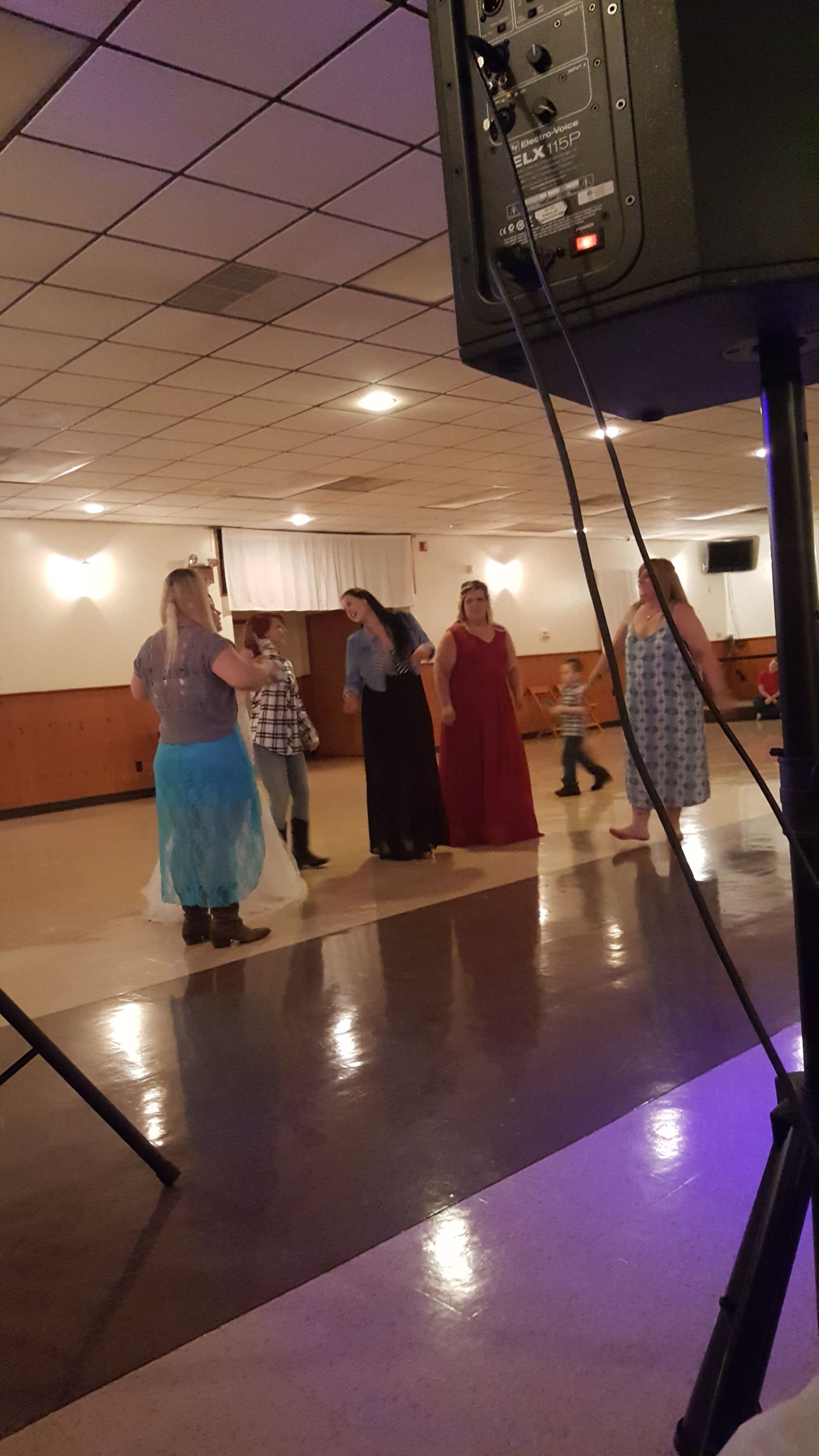 People standing and talking in a banquet hall near a large speaker and reflective dance floor.