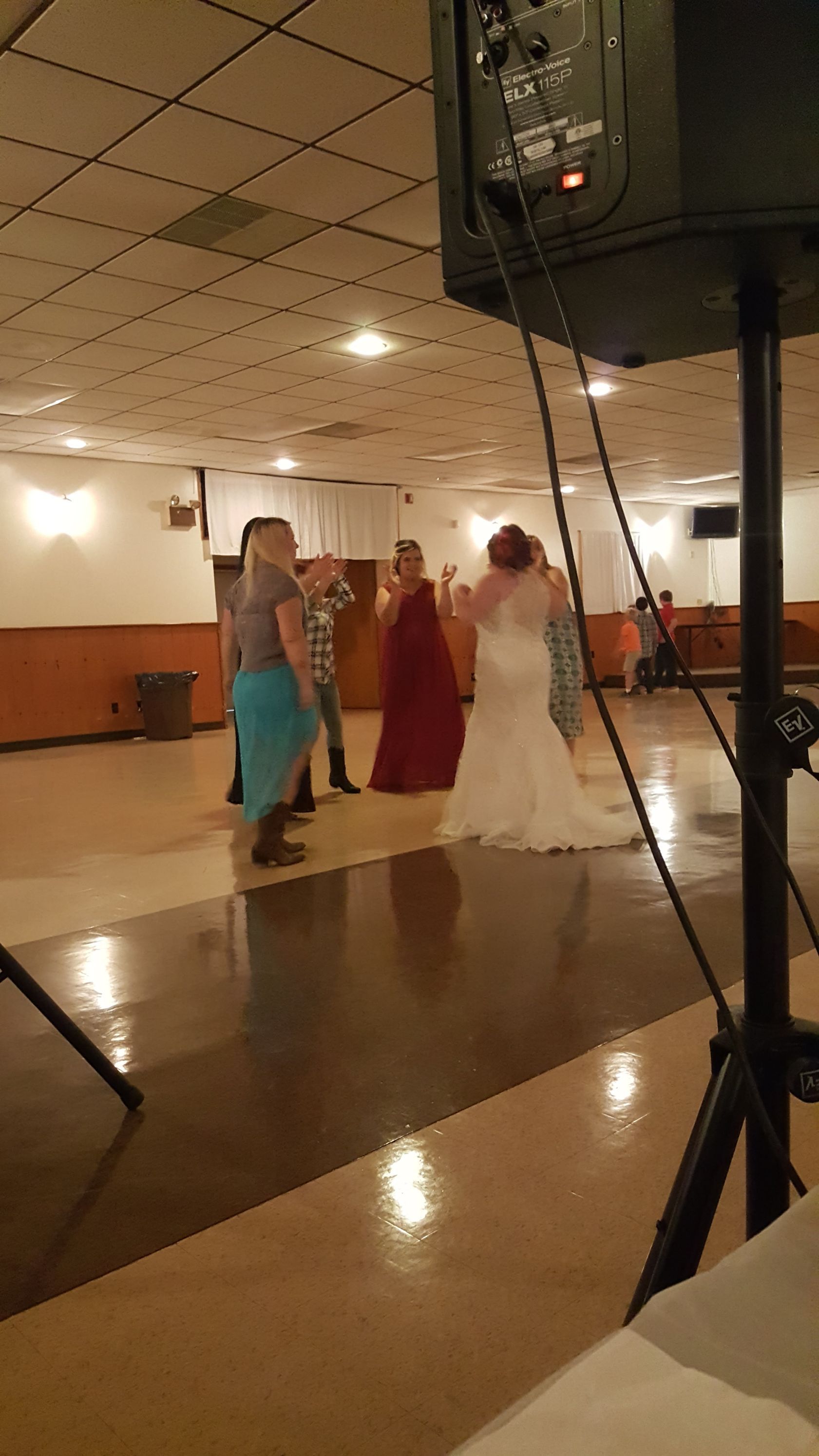 People dancing at a banquet hall reception, with one in a white dress and another in a red dress.