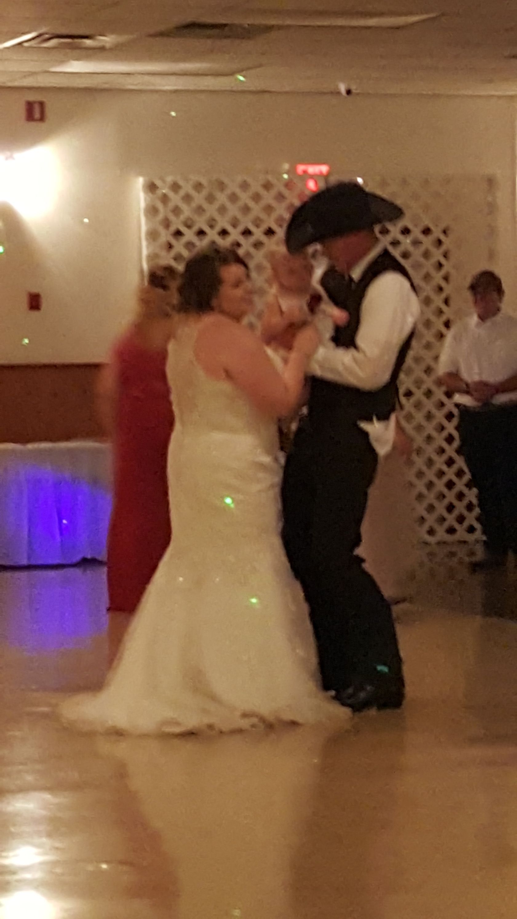 Couple dancing at a formal event, bride in white dress and groom in black vest, in a banquet hall