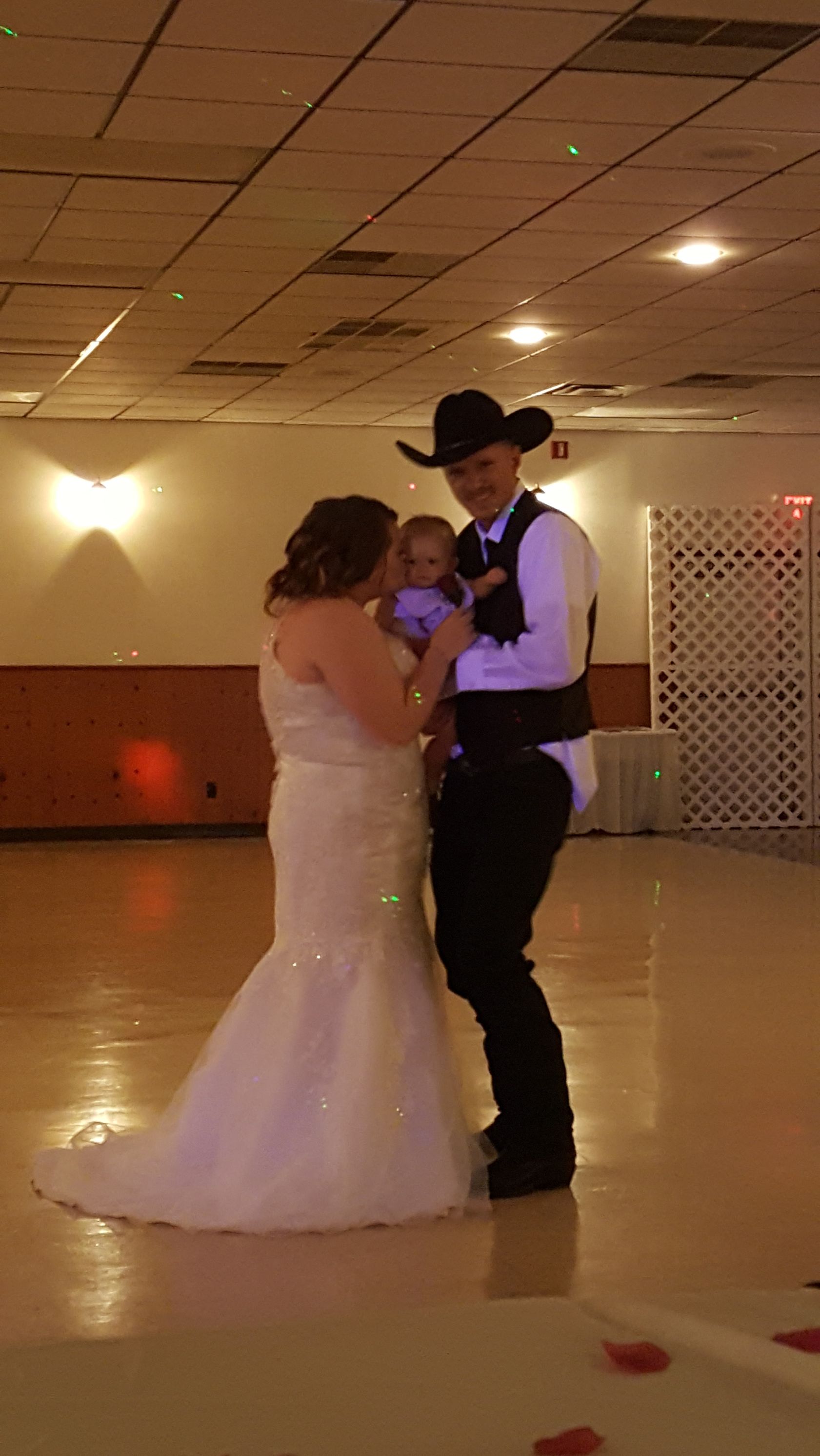 Couple slow dancing in a hall, bride in a white gown and partner in a black hat and vest