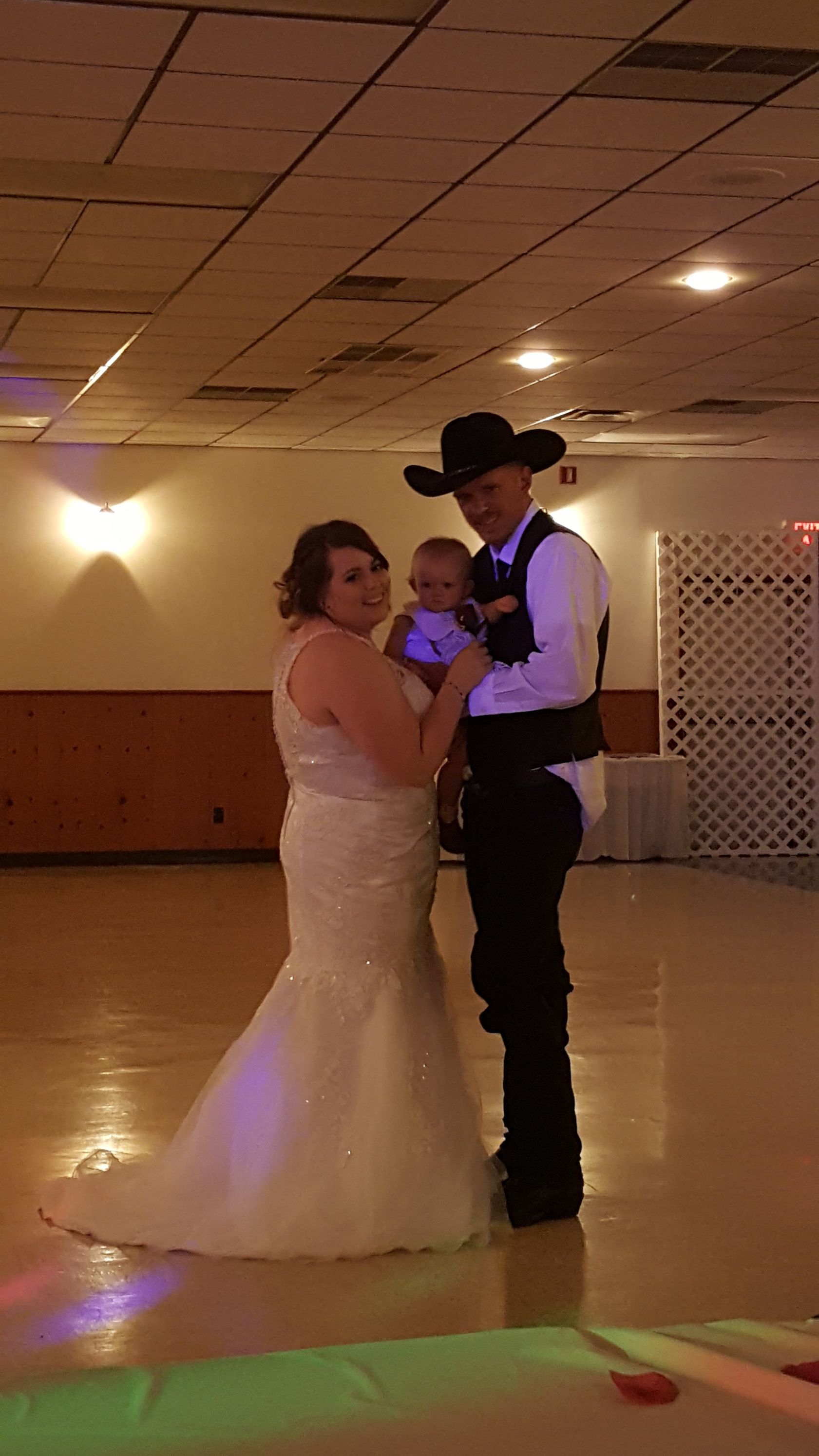 Couple in formal attire slow dancing at a reception hall, with colorful lights on the floor.