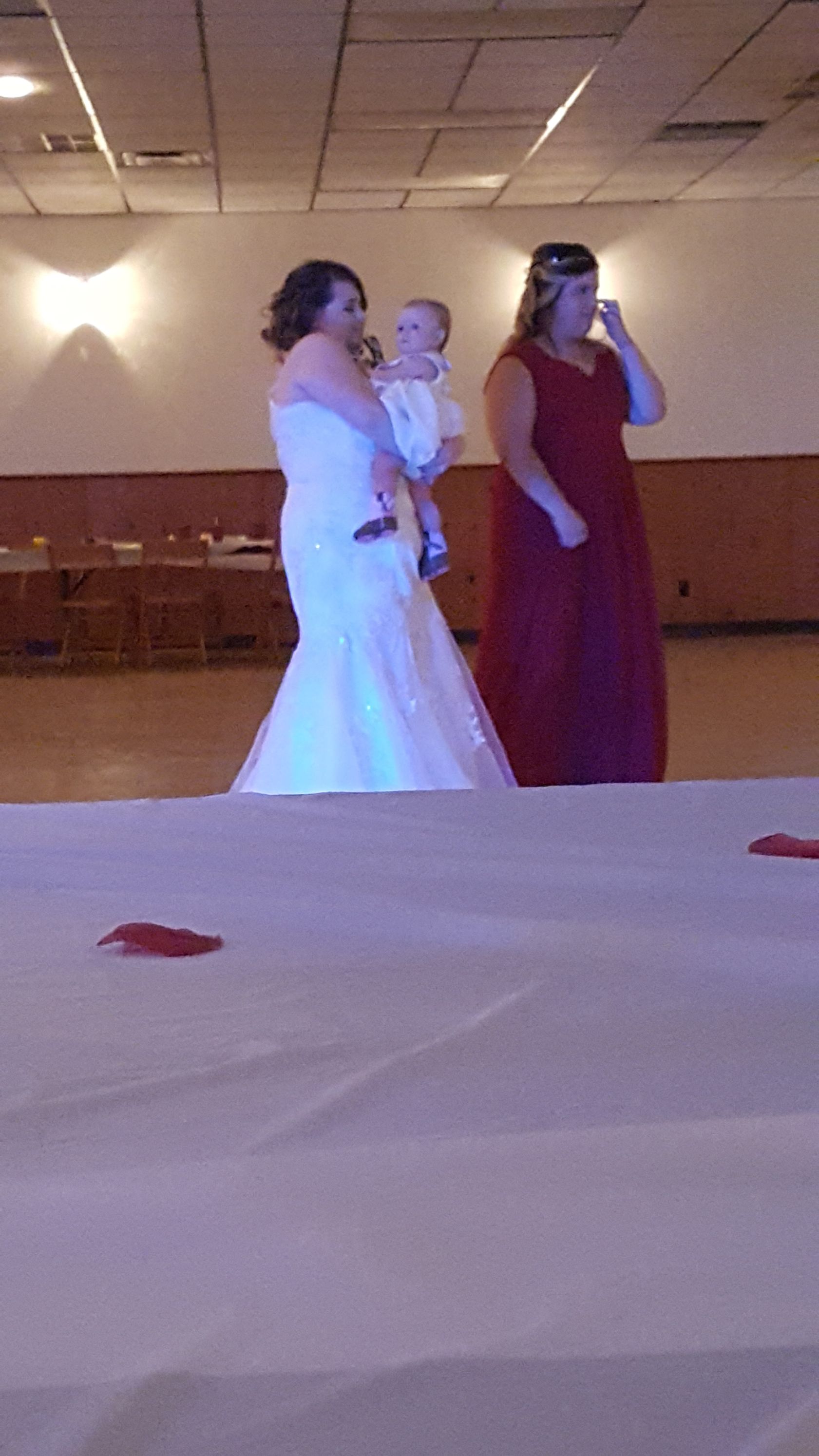 Three women in formal dresses posing in a banquet hall, one holding a phone near her face.