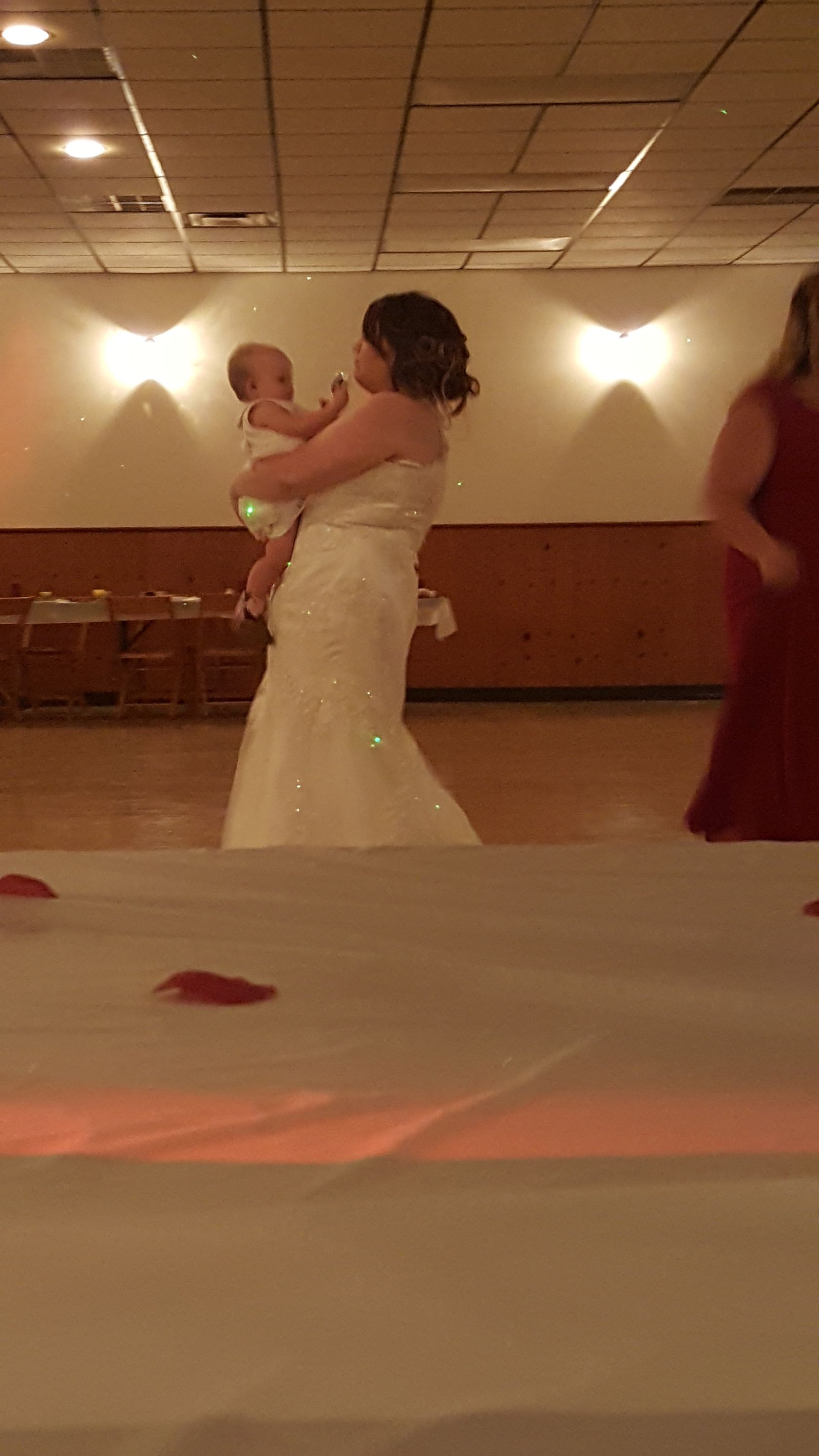 Bride in a white gown dancing in a warmly lit reception hall, with a table in the foreground.