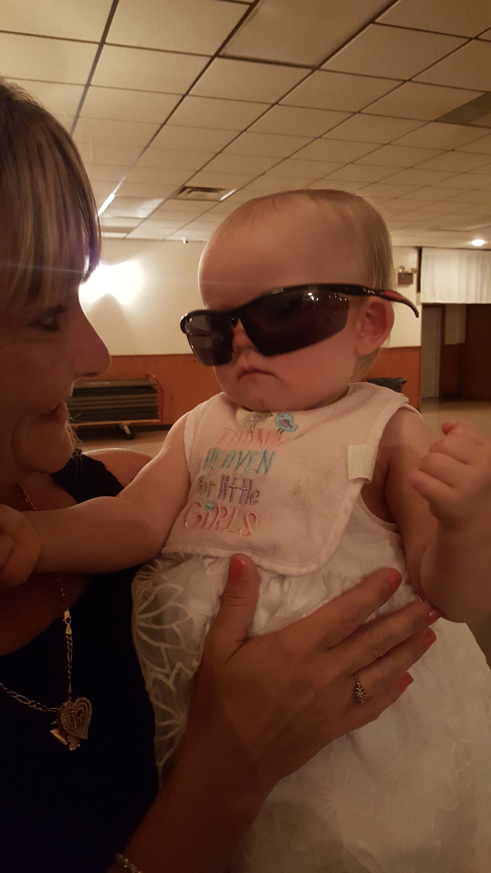 Baby wearing sunglasses being held by an adult in a warmly lit indoor room