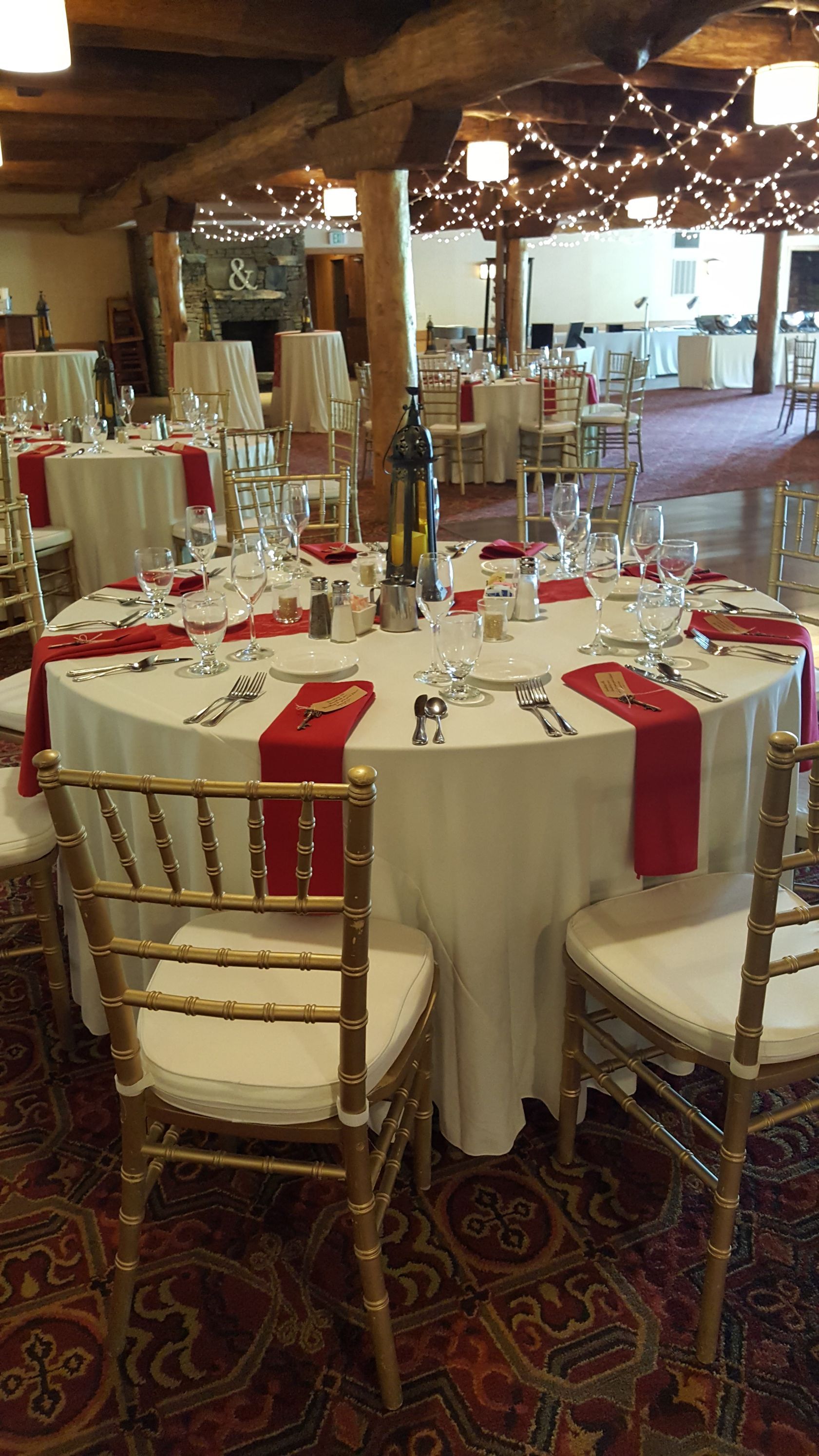 Decorated banquet hall with round tables, red-and-white tablecloths, and gold chairs arranged for an event
