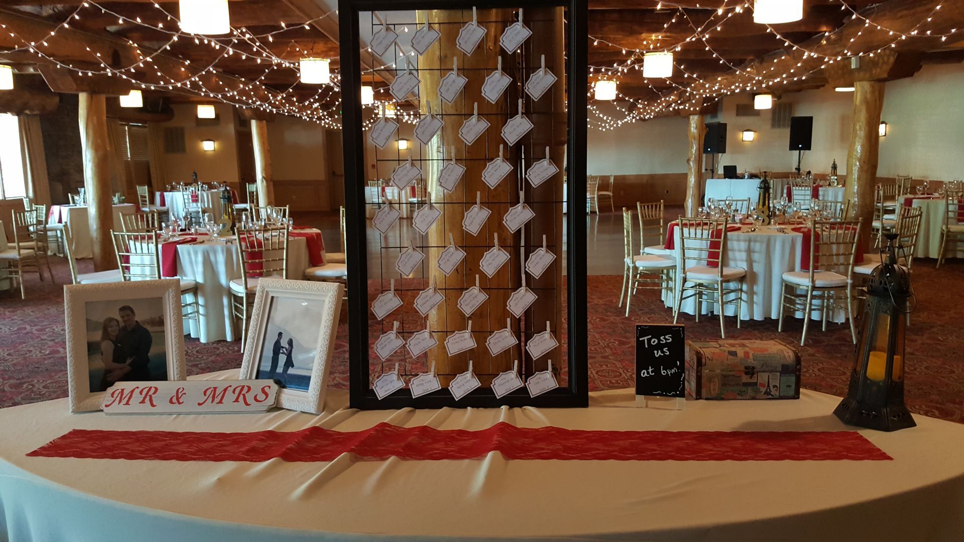 Decorated banquet hall display with white chairs, tall board centerpiece, red carpet, and string lights