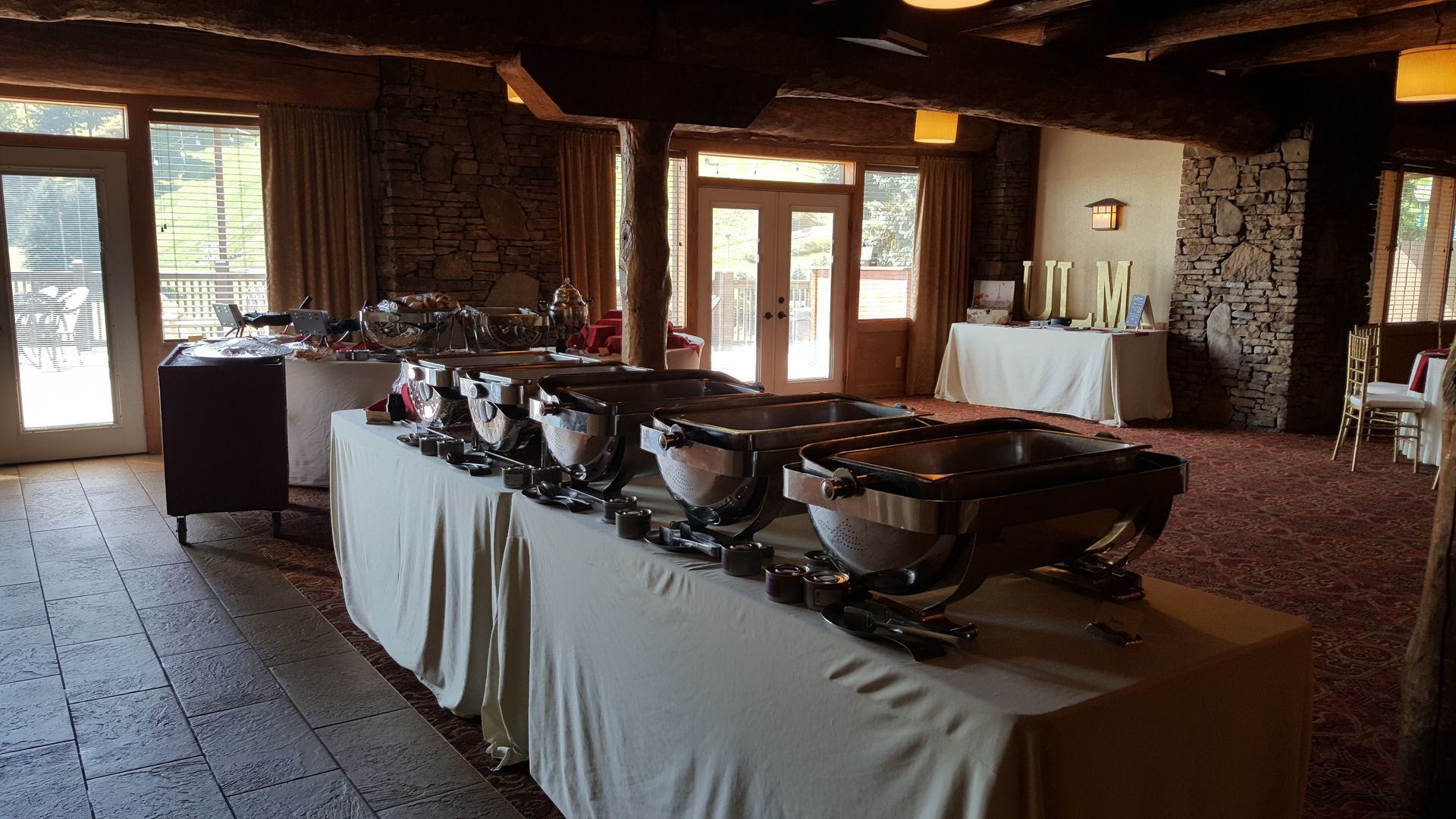 Buffet table with covered dishes in a rustic lodge dining room near large windows