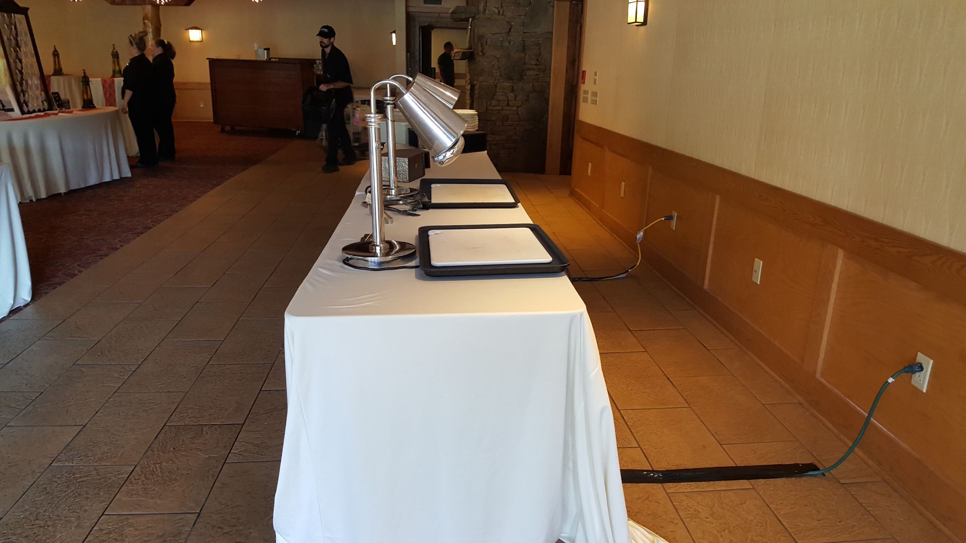 Tables with display monitors in a banquet hall hallway, with a person standing in the background.