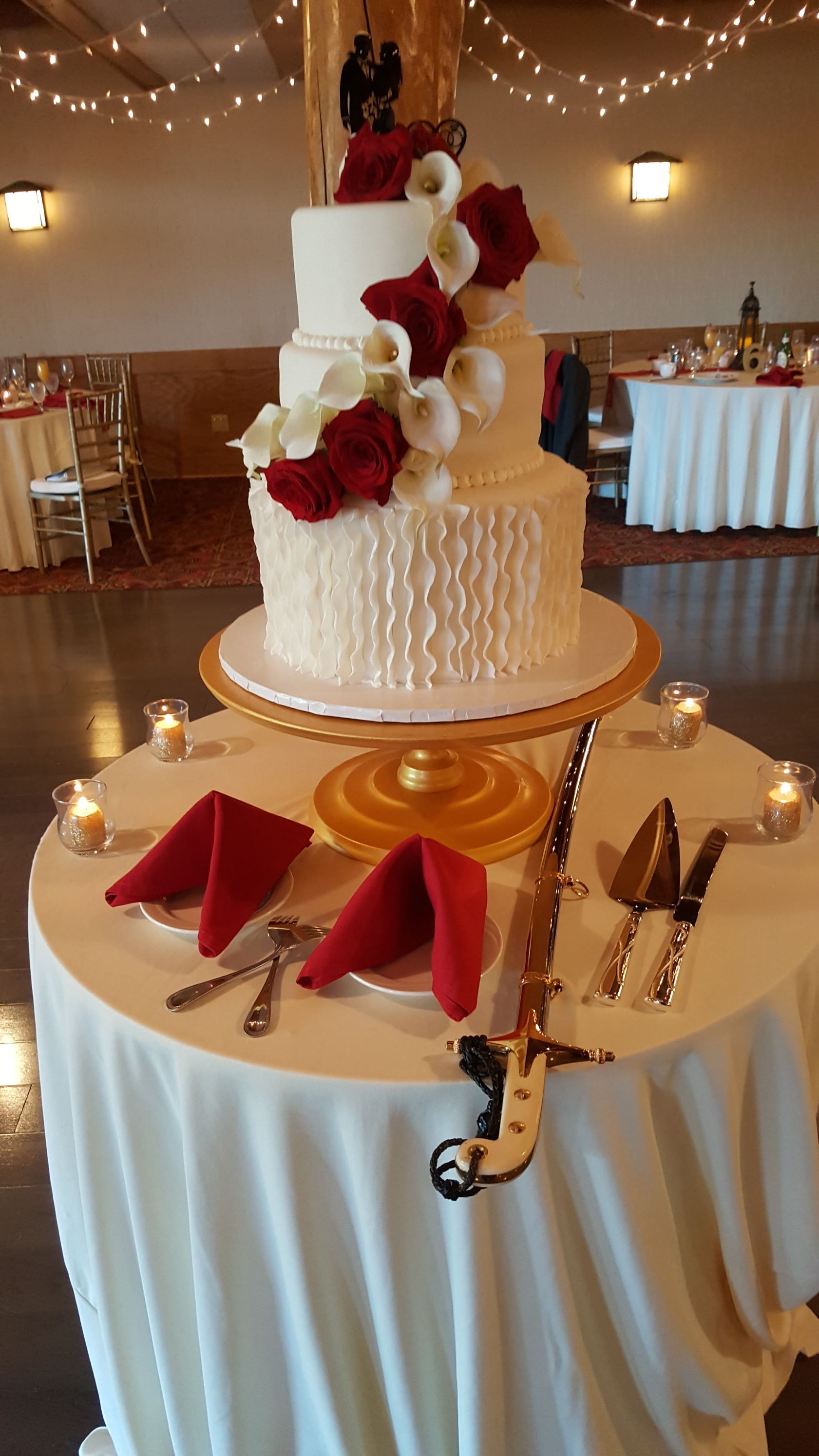Two-tiered white wedding cake with red roses on a round table set with folded red napkins and candles