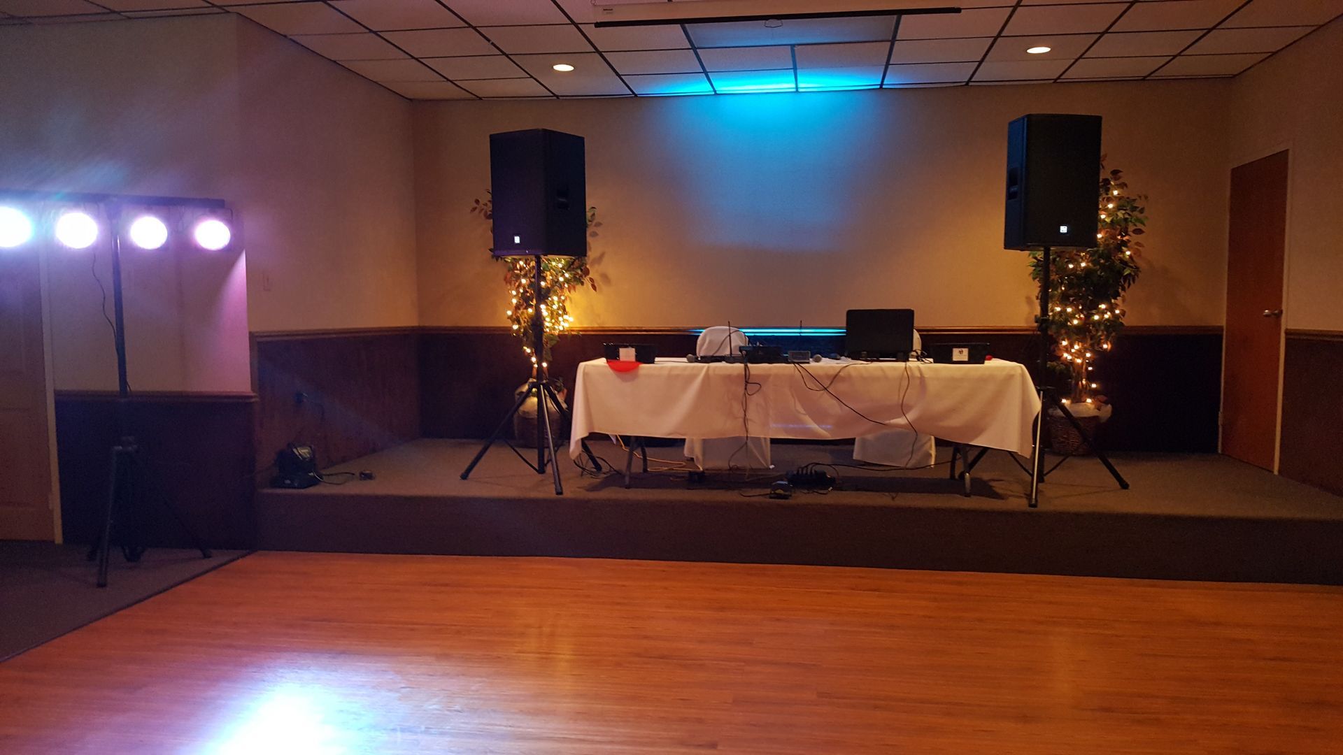 Empty banquet hall with a small stage, DJ table, speakers, and purple lights