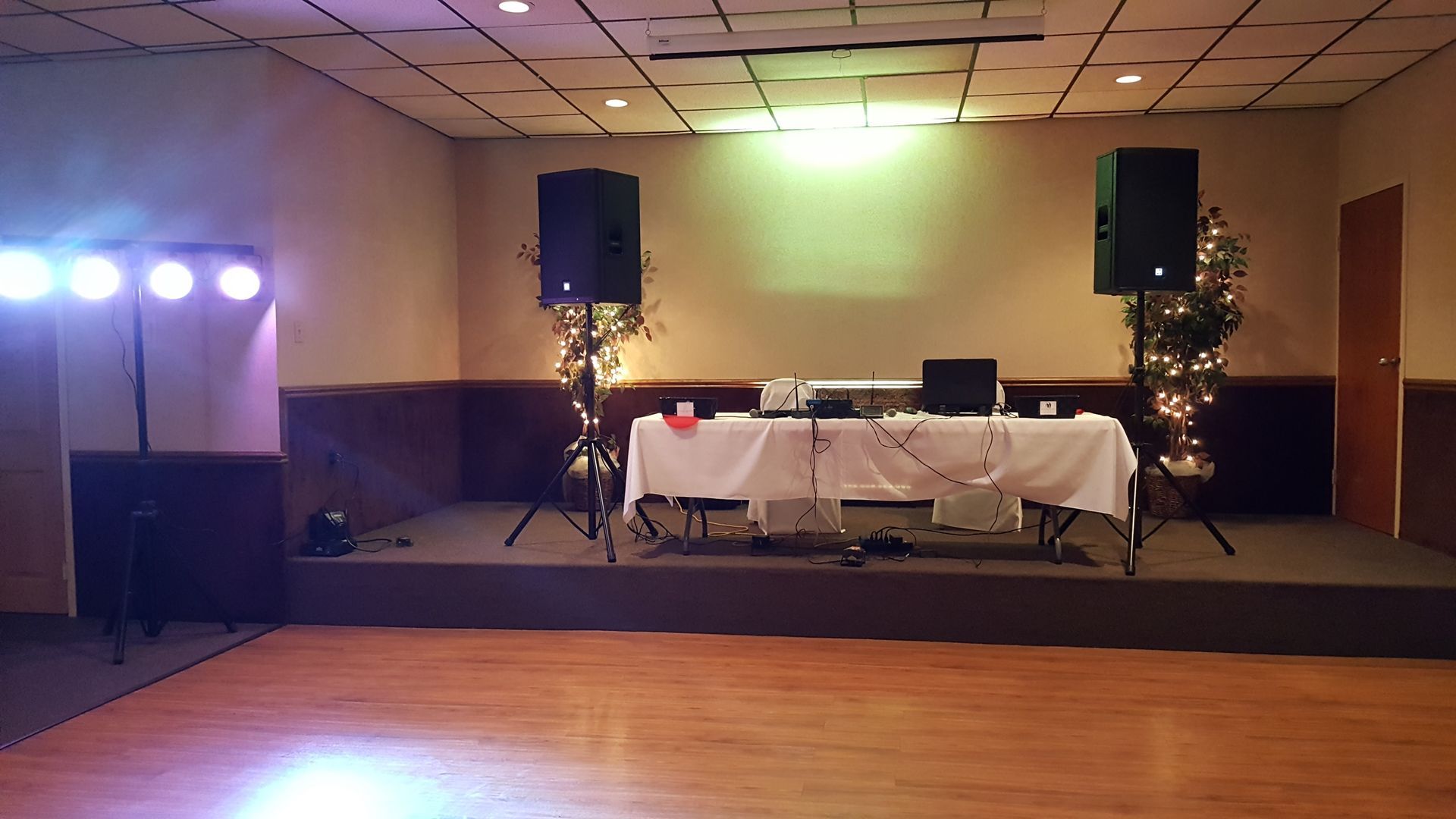 Decorated banquet hall stage with DJ table, speakers, and purple-green lighting