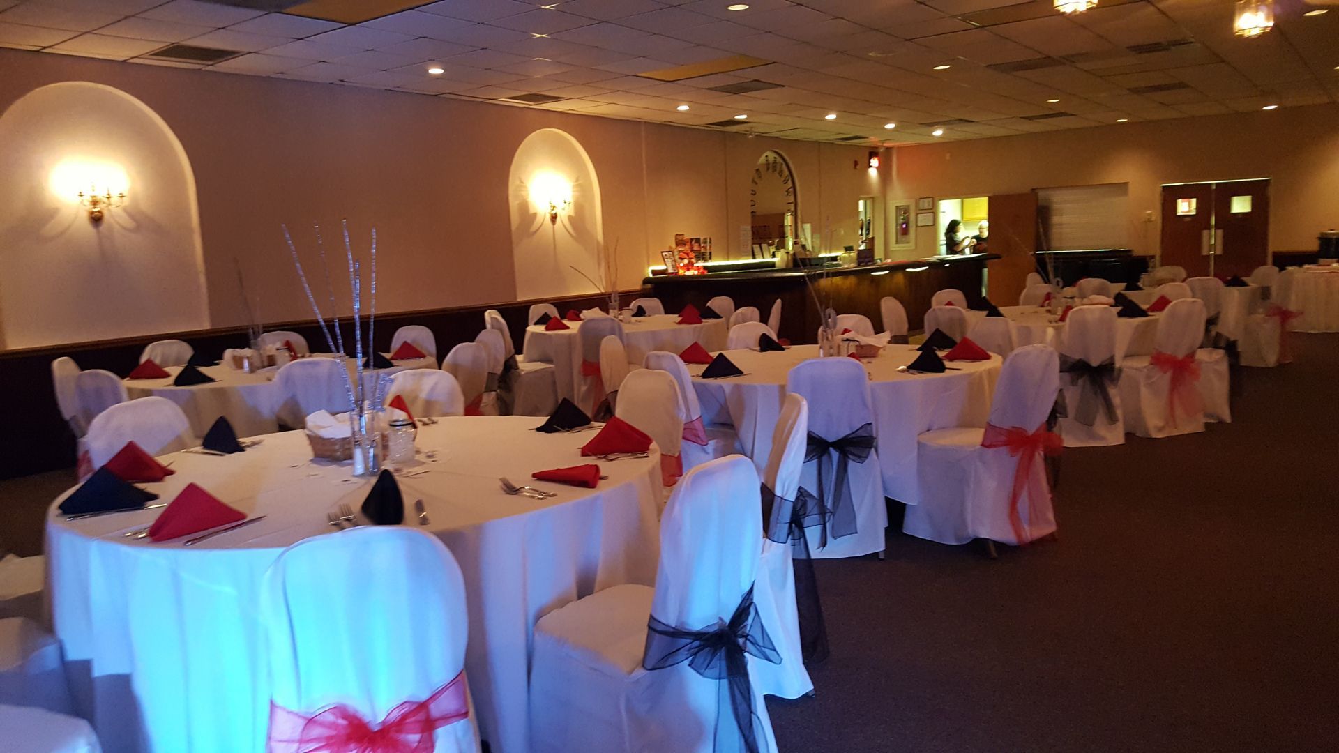 Decorated banquet hall with round tables, white chair covers, and red napkins set for an event