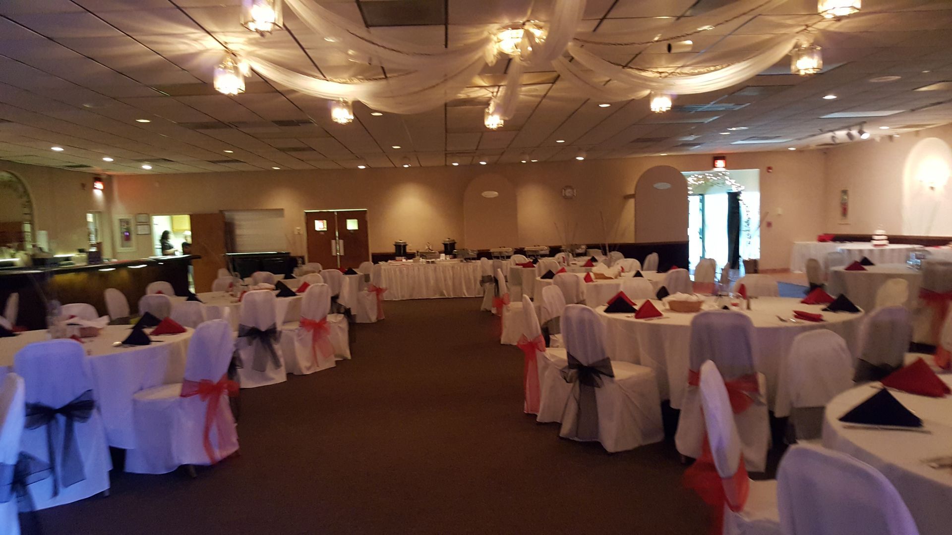 Empty banquet hall with round tables, white chair covers, pink sashes, and draped ceiling lights