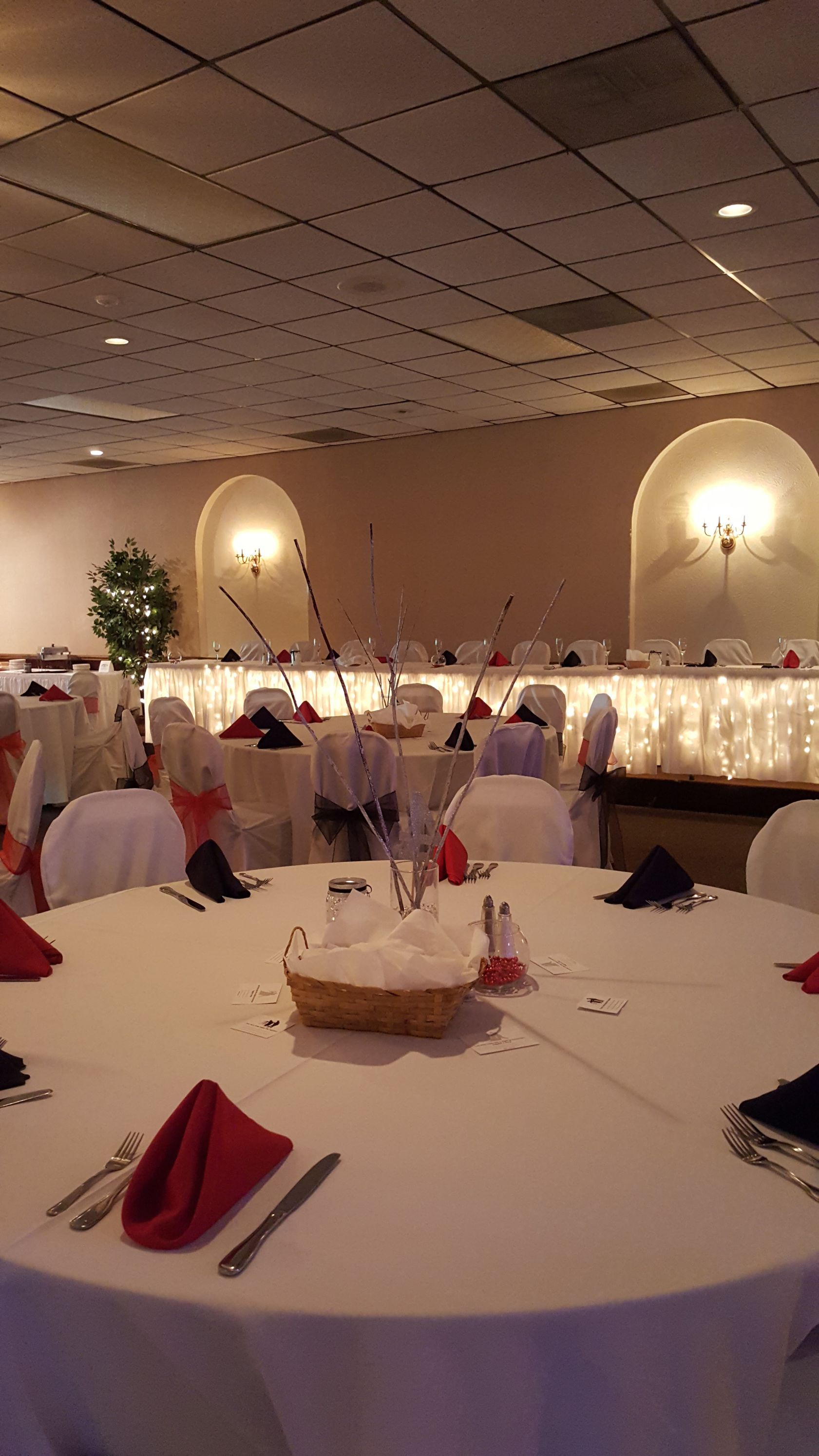 Round banquet hall with white tablecloths, red napkins, lit wall sconces, and decorated tables around the room