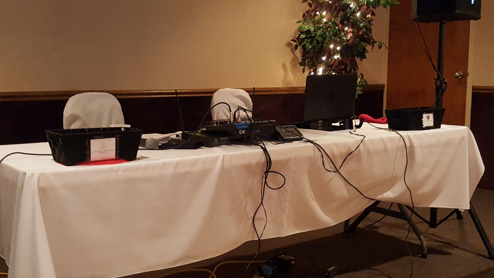 Conference table with laptops, cables, and covered devices on a white tablecloth in a room