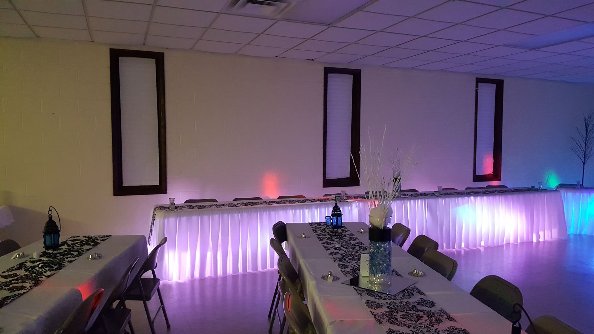 Decorated banquet hall with long tables, black chairs, and purple LED lights along the wall and tables