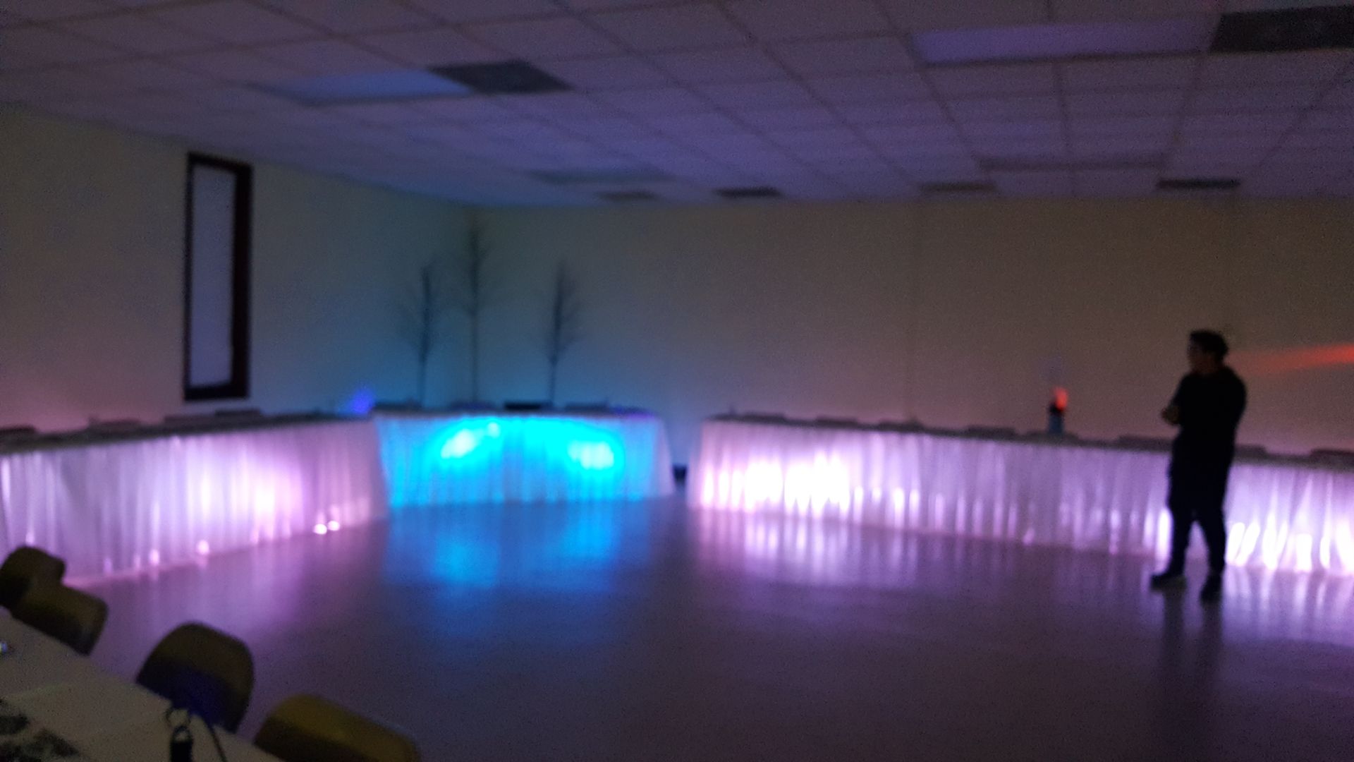 Dim hall with glowing blue and purple LED-lit draped walls and one person standing on the right