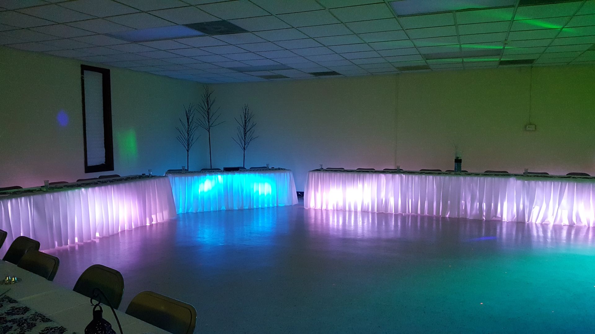 Empty room with draped tables and purple-blue LED lighting along the walls and floor