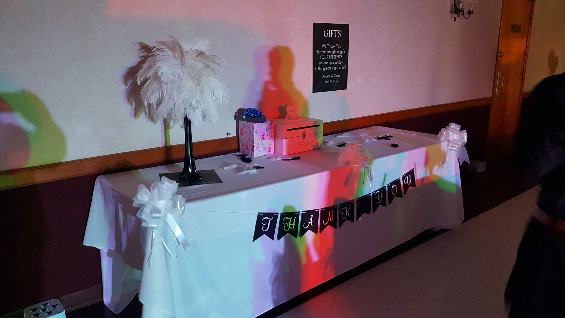 Decorated table with white feather centerpiece and pink accents in a dim hallway event setup