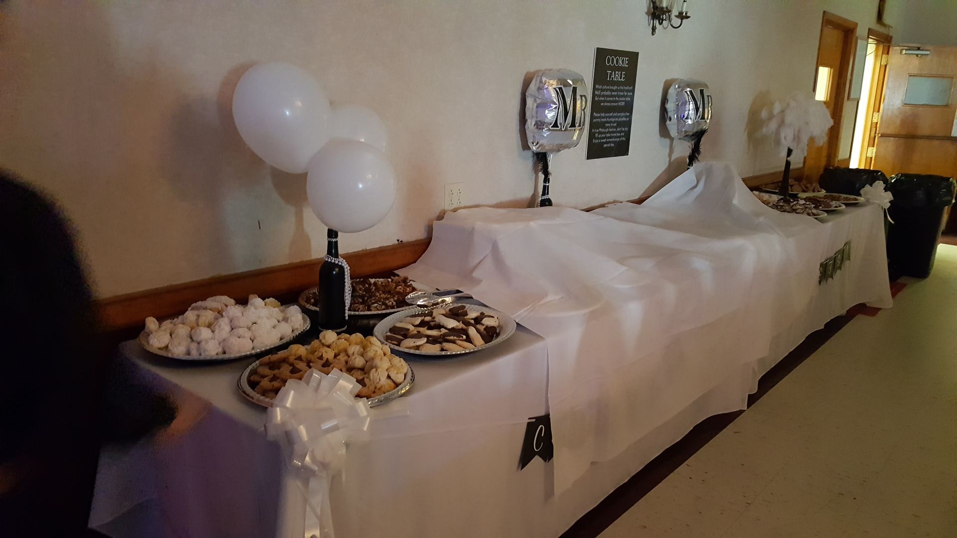 Buffet table with white tablecloth, balloons, trays of pastries, and silver chafing dishes at an indoor event