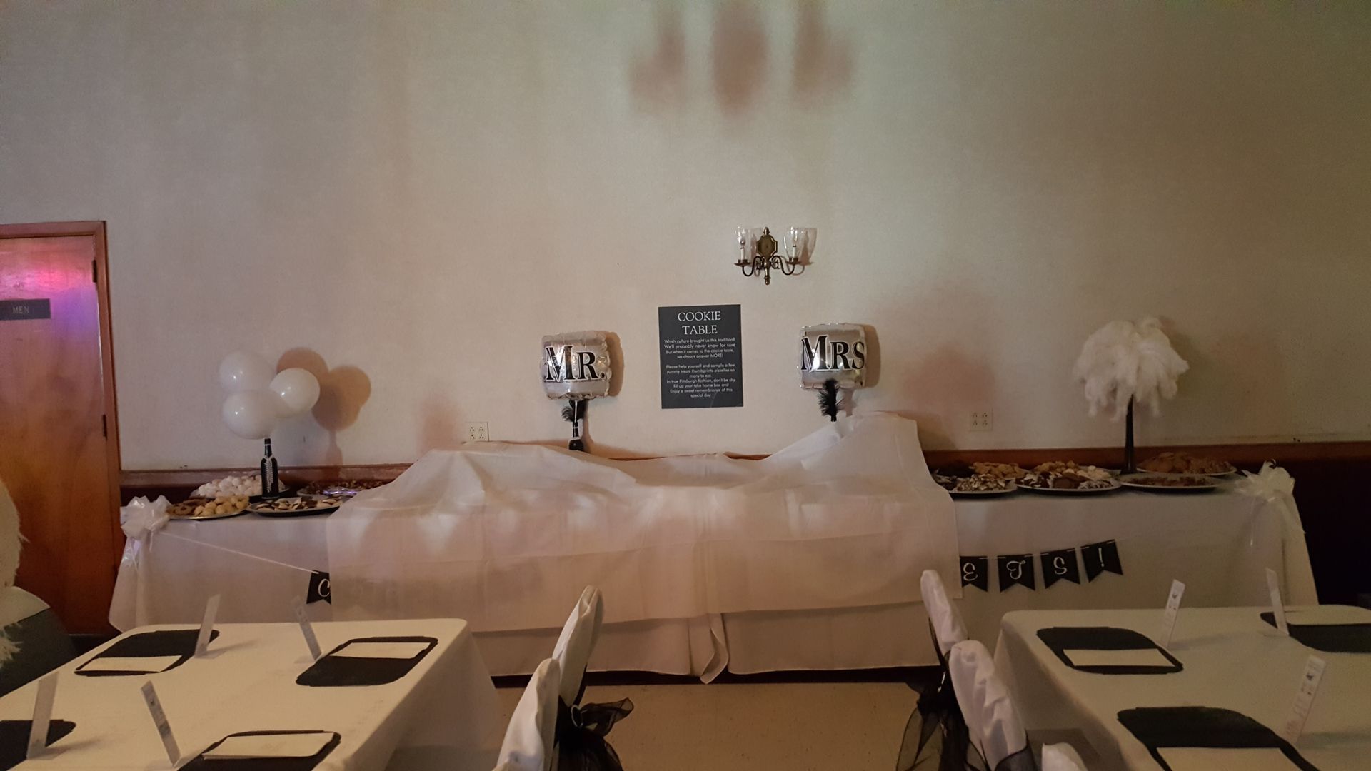 Decorated banquet table with white cloths, plates, napkins, and centerpieces in a softly lit hall