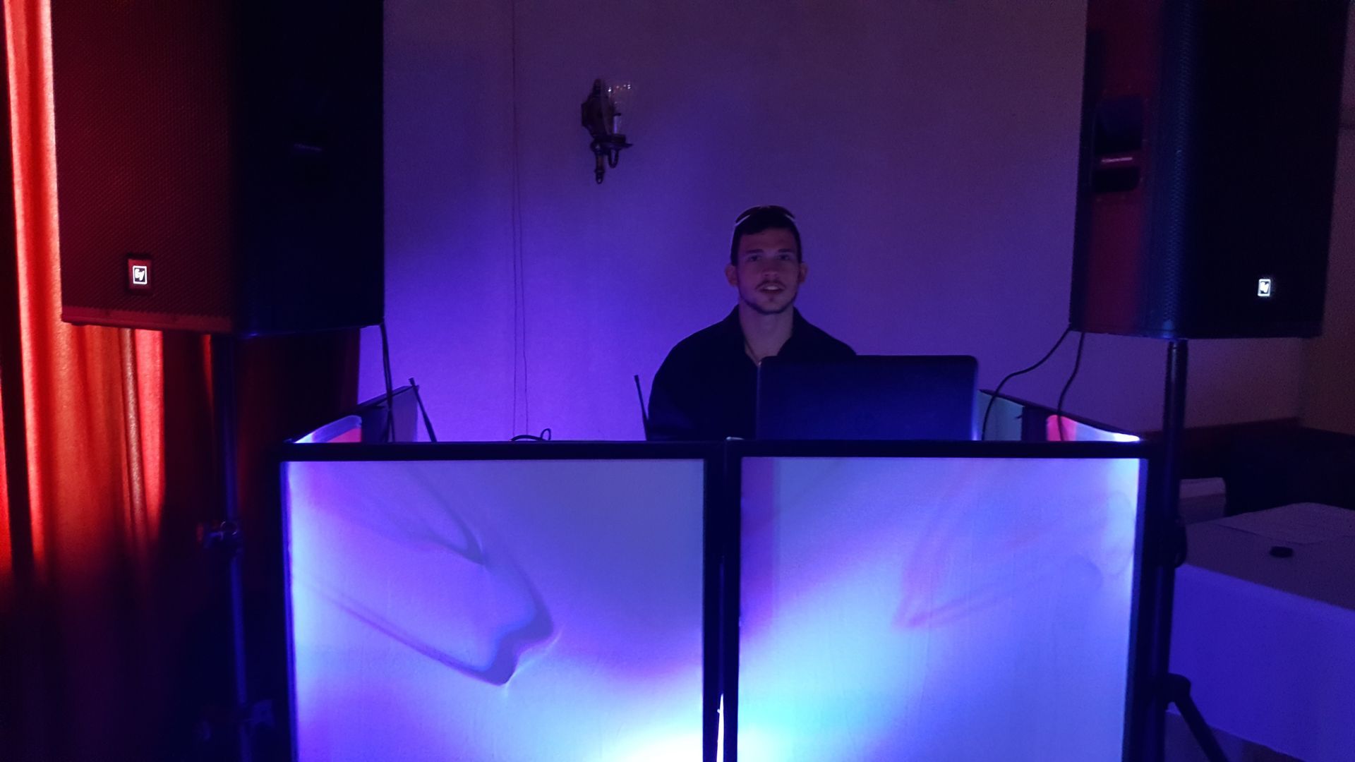 Person behind glowing blue DJ booth in a dim room with purple lighting