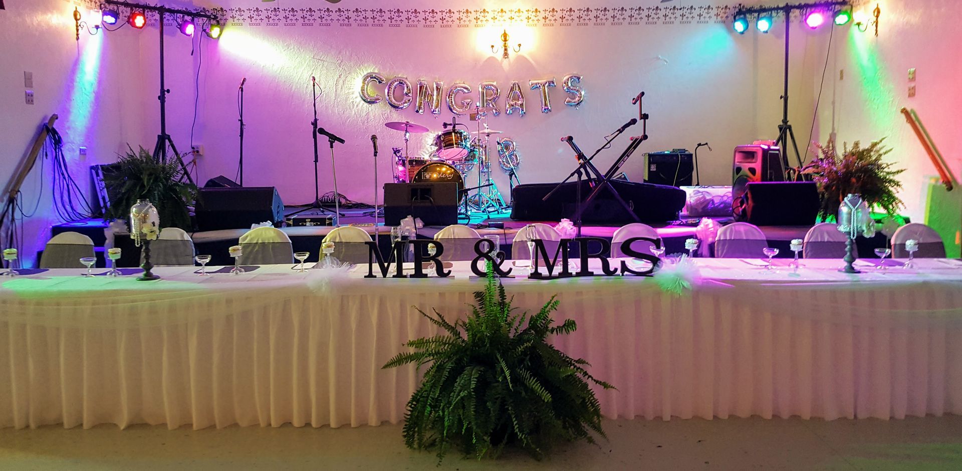 Decorated wedding stage with DJ equipment, colorful lights, and “Mr & Mrs” sign in front