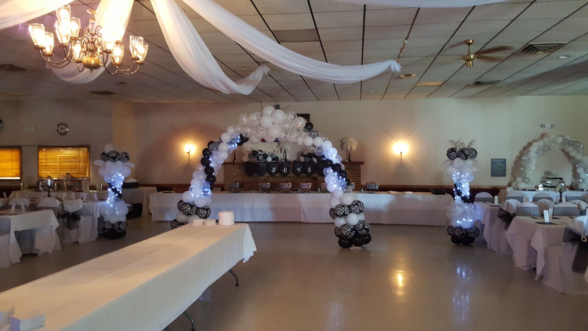 Decorated banquet hall with white drapes, floral centerpieces, and tables set for an event