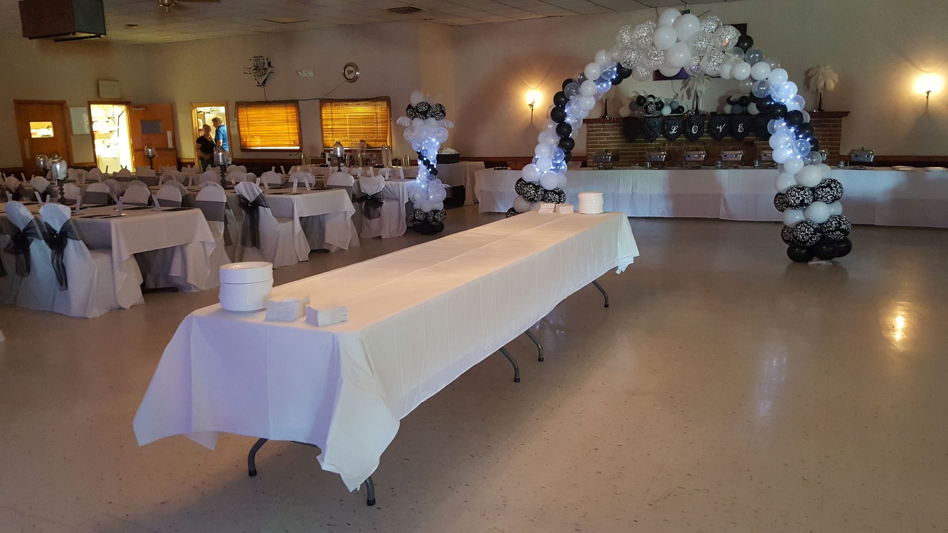 Banquet hall with white tablecloth tables and a white-and-black balloon arch decorated with flowers