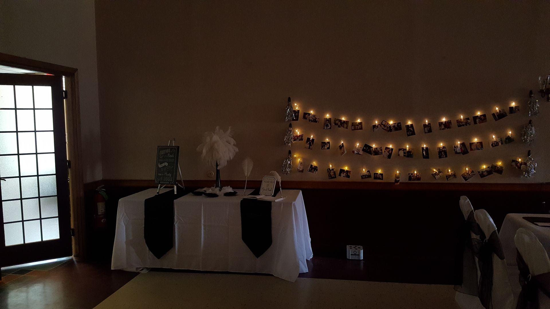 Decorated indoor table with black-and-white linens and warm string lights on the wall behind it