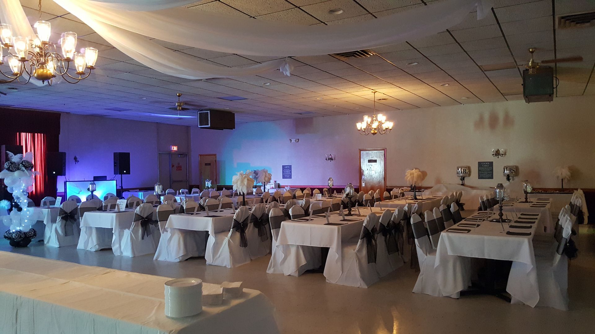 Banquet hall set for a formal event with round tables, white chairs, and blue-purple stage lighting