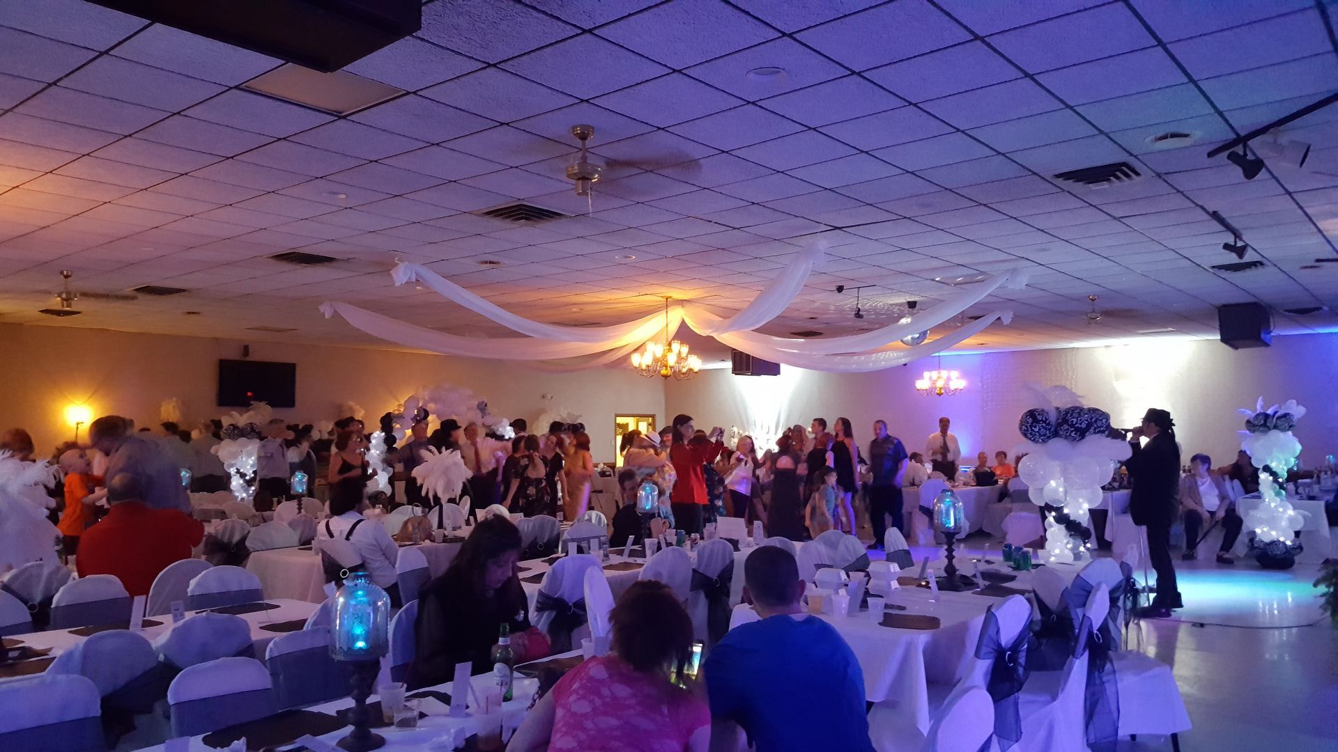 Banquet hall with guests seated at round tables under purple and warm lighting, facing a central dance floor