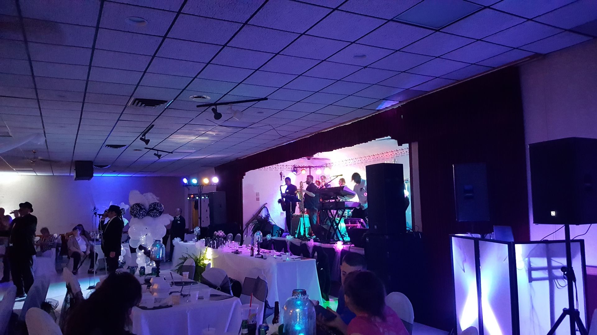 Indoor party with live band on a lit stage and guests seated at tables in purple lighting