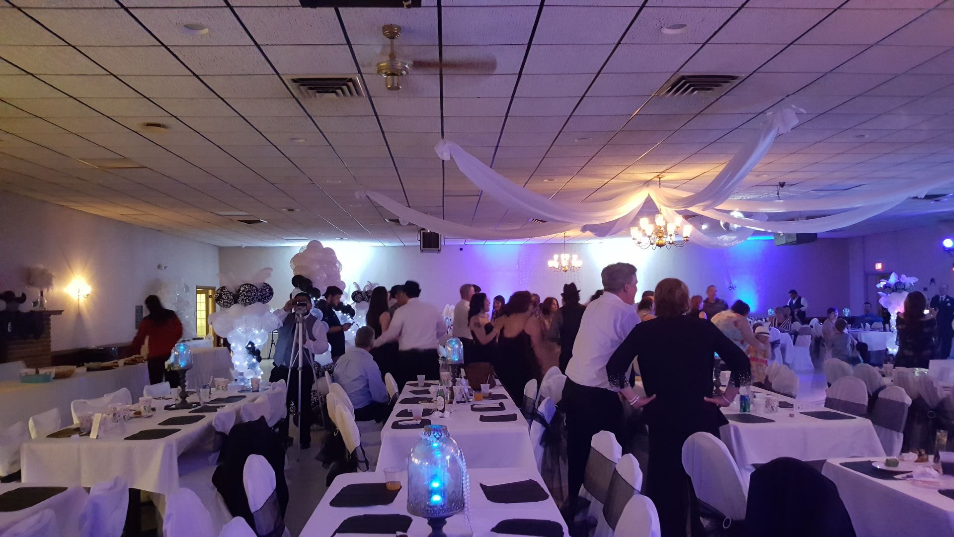 Guests mingling at a decorated indoor banquet with blue-purple lighting and long dining tables