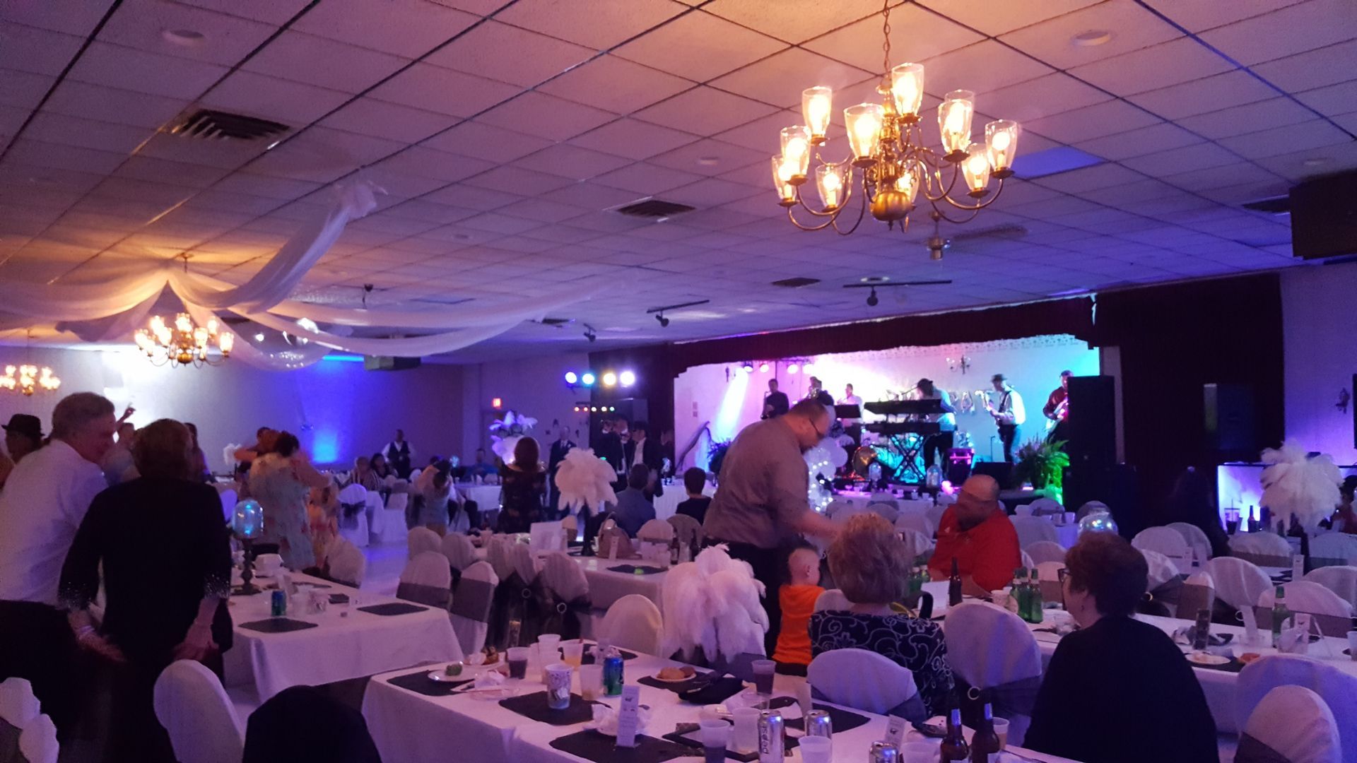 Banquet hall with guests seated at round tables, a lit dance floor, and purple stage lighting