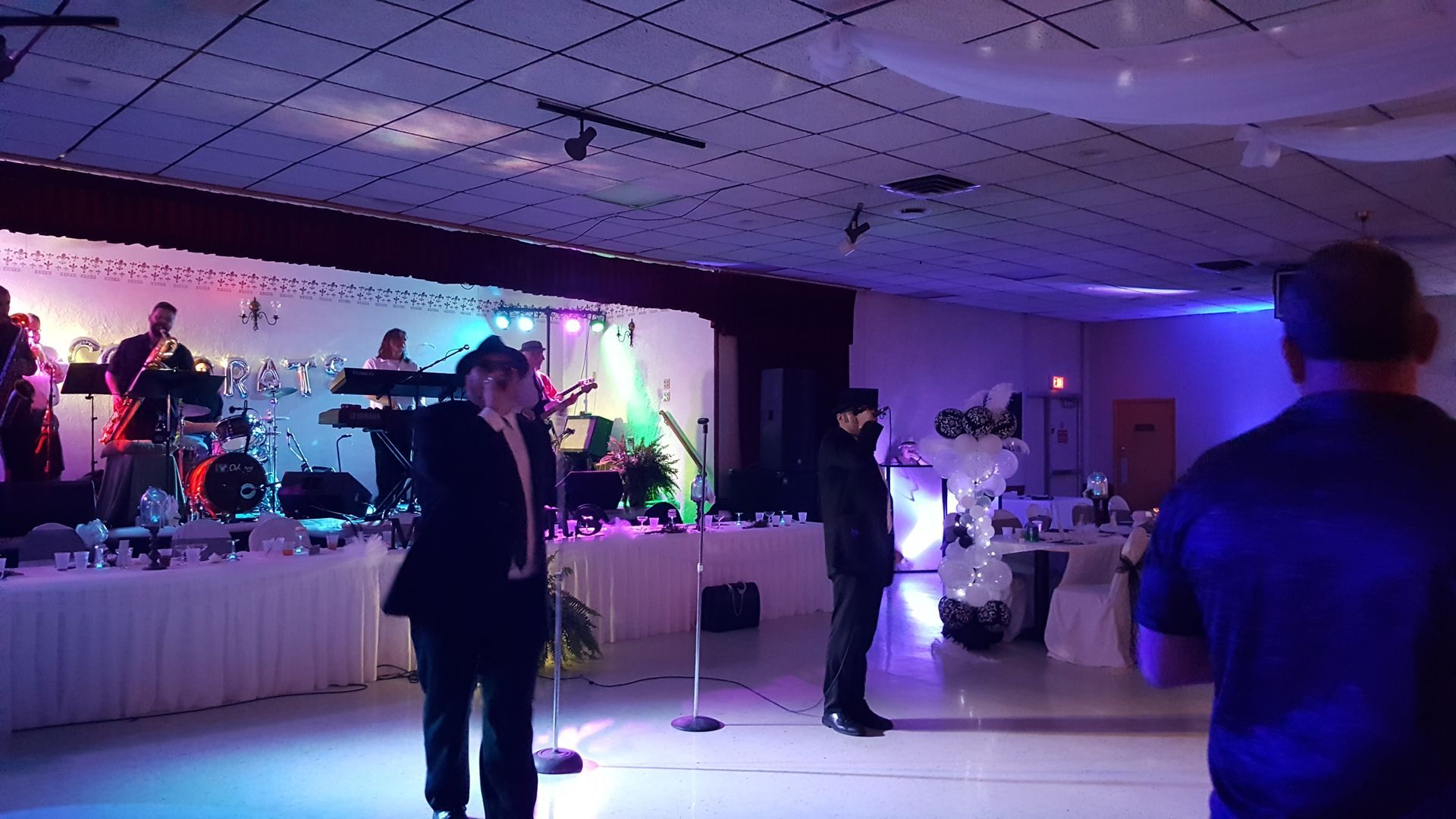 People mingling on a purple-lit dance floor beside a stage at an indoor event.