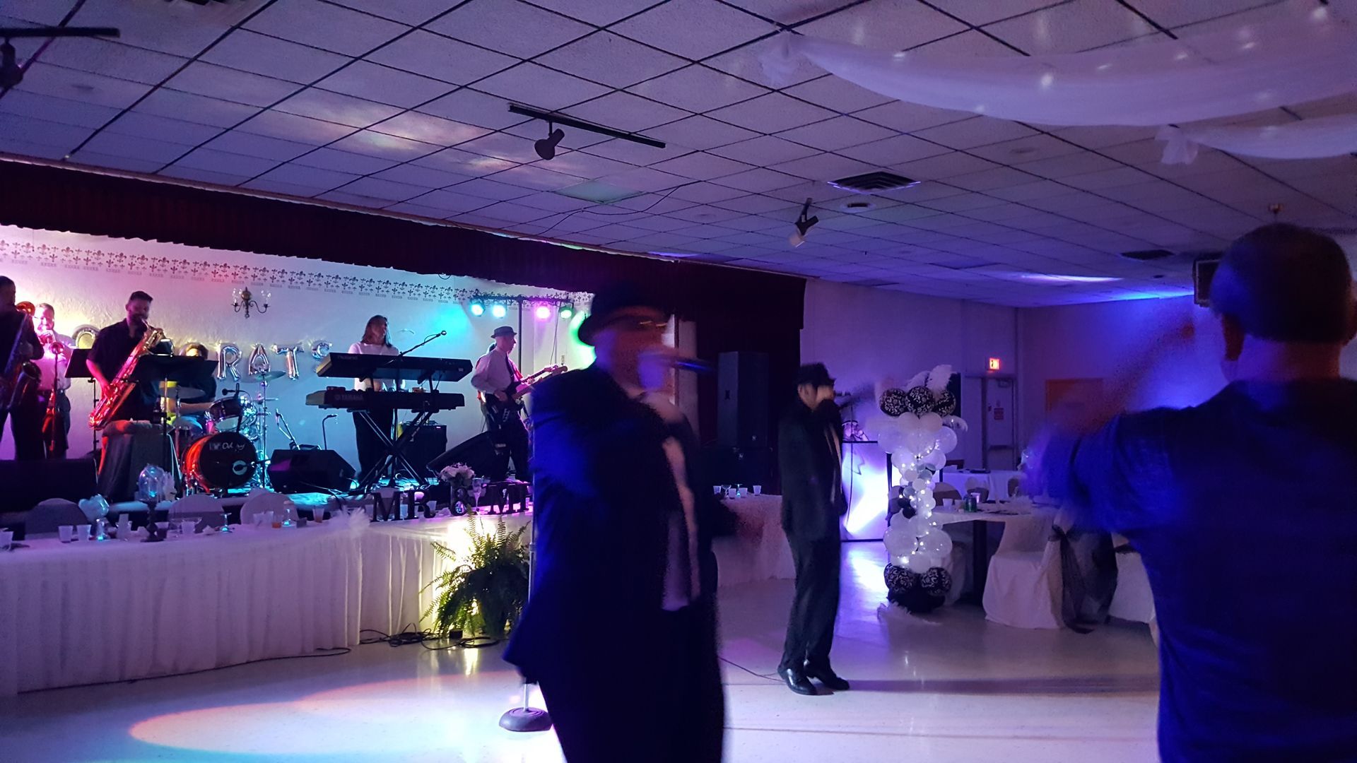 Band performing on a lit stage while guests dance in a dim banquet hall