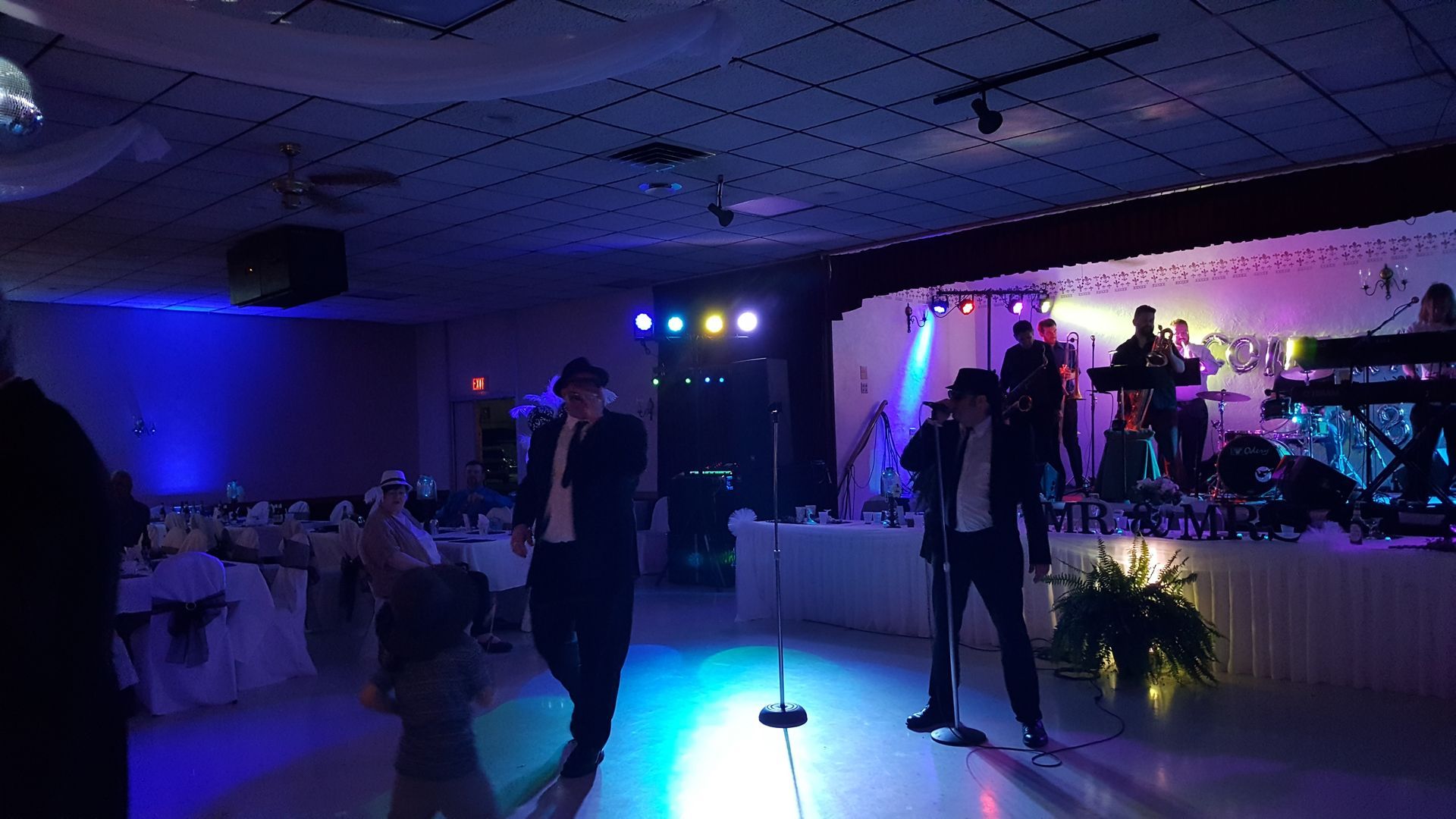 Live band performing on a dimly lit dance floor in a banquet hall with blue and purple lights