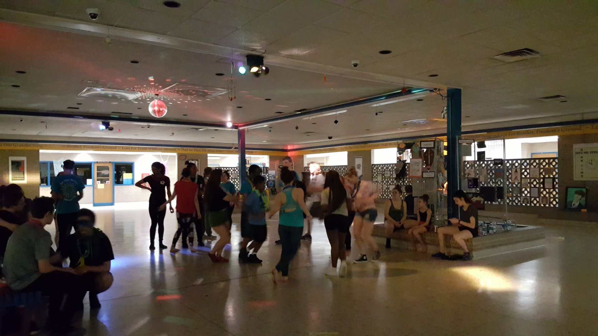 People gathered in a dimly lit indoor hall, standing and sitting near a central open floor.