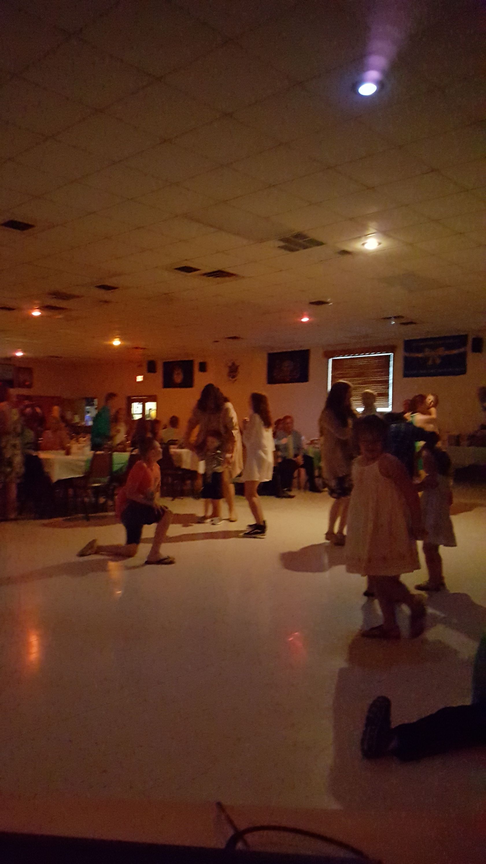 Dimly lit indoor dance floor with several people dancing under colored ceiling lights.