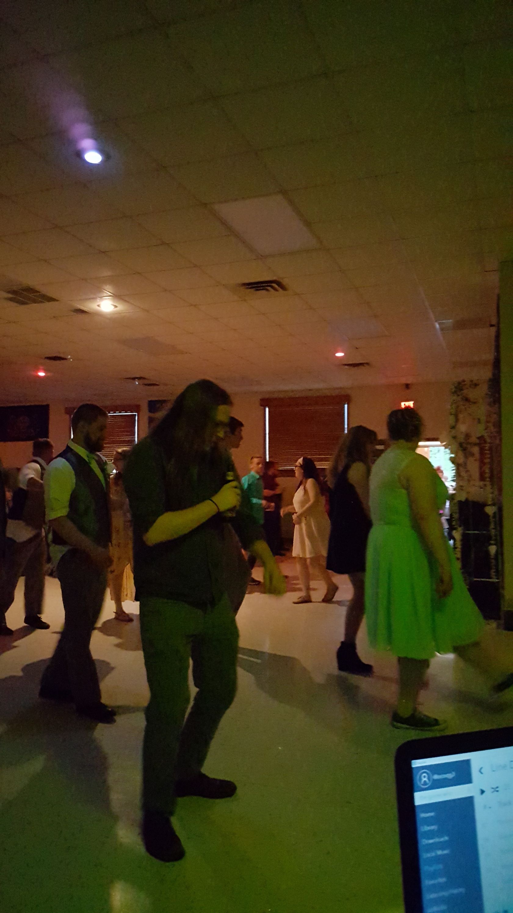 People dancing in a dimly lit indoor hall, with green and white lights.