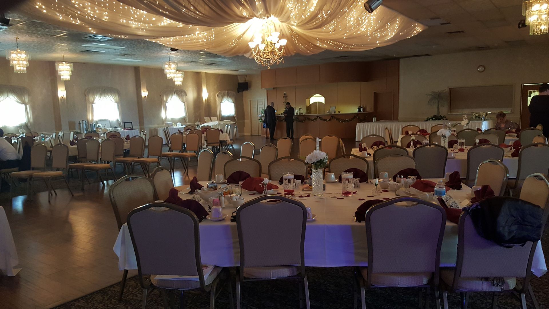 Banquet hall with round dining tables, purple chairs, and warm chandeliers under draped ceiling decor