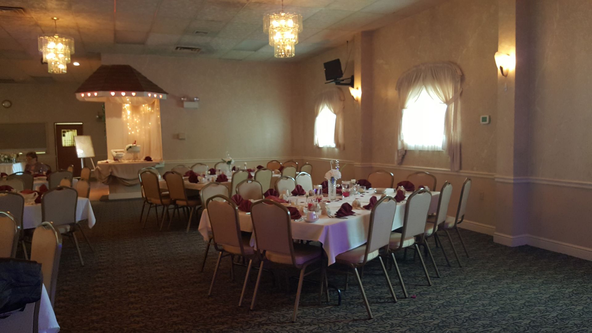 Banquet hall with round tables and chairs set for an event, lit by chandeliers and wall sconces.
