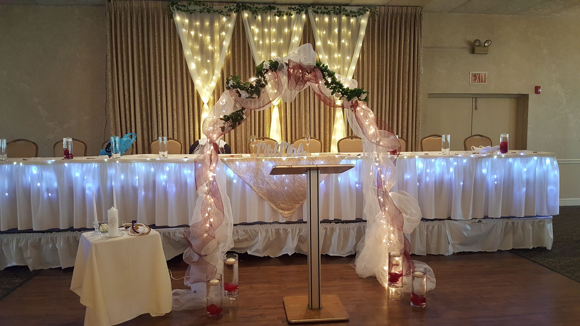 Decorated wedding reception table with white drapes, fairy lights, and floral arch centerpiece